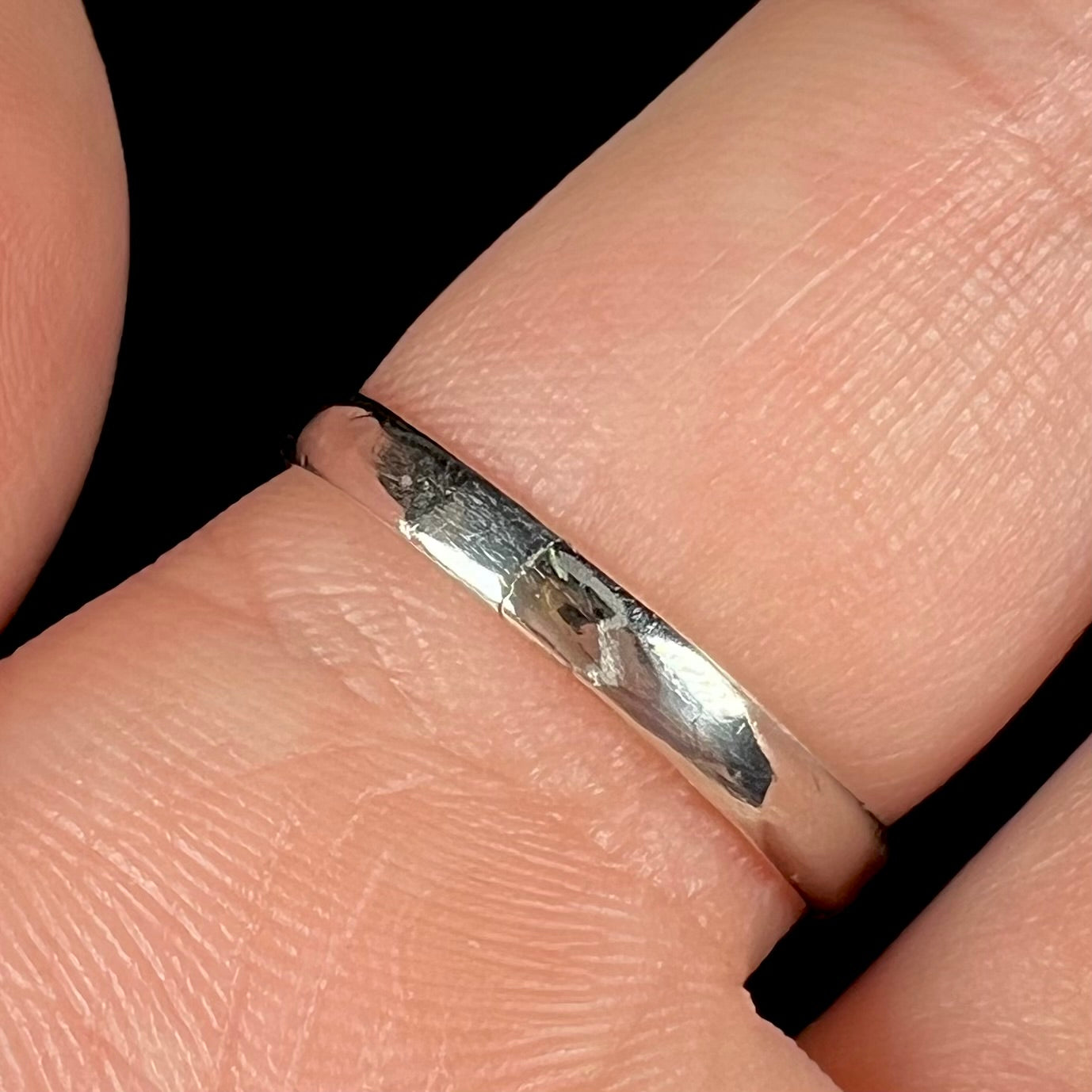The bottom of a cracked shank on a sterling silver ring, worn on a finger and shown close-up.