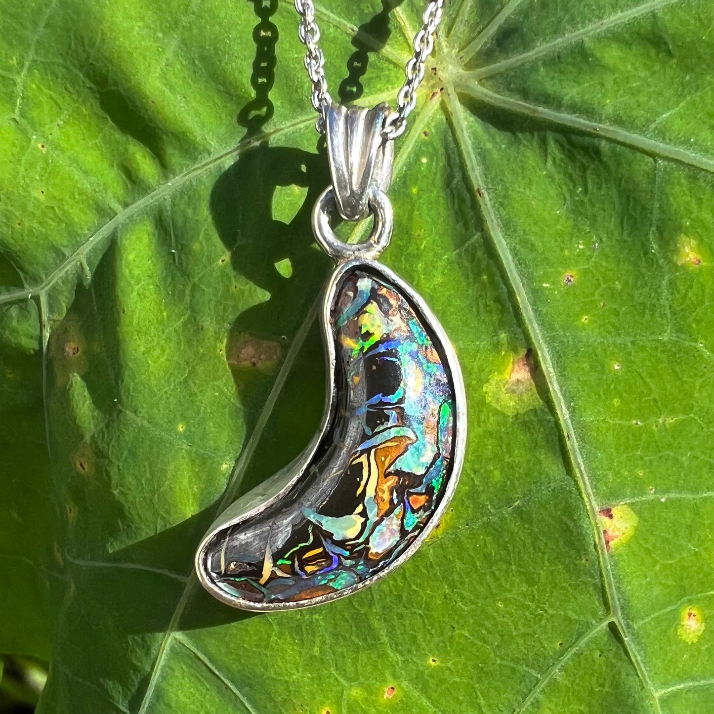 A sterling silver necklace set with a natural Koroit boulder opal shaped like a crescent moon.