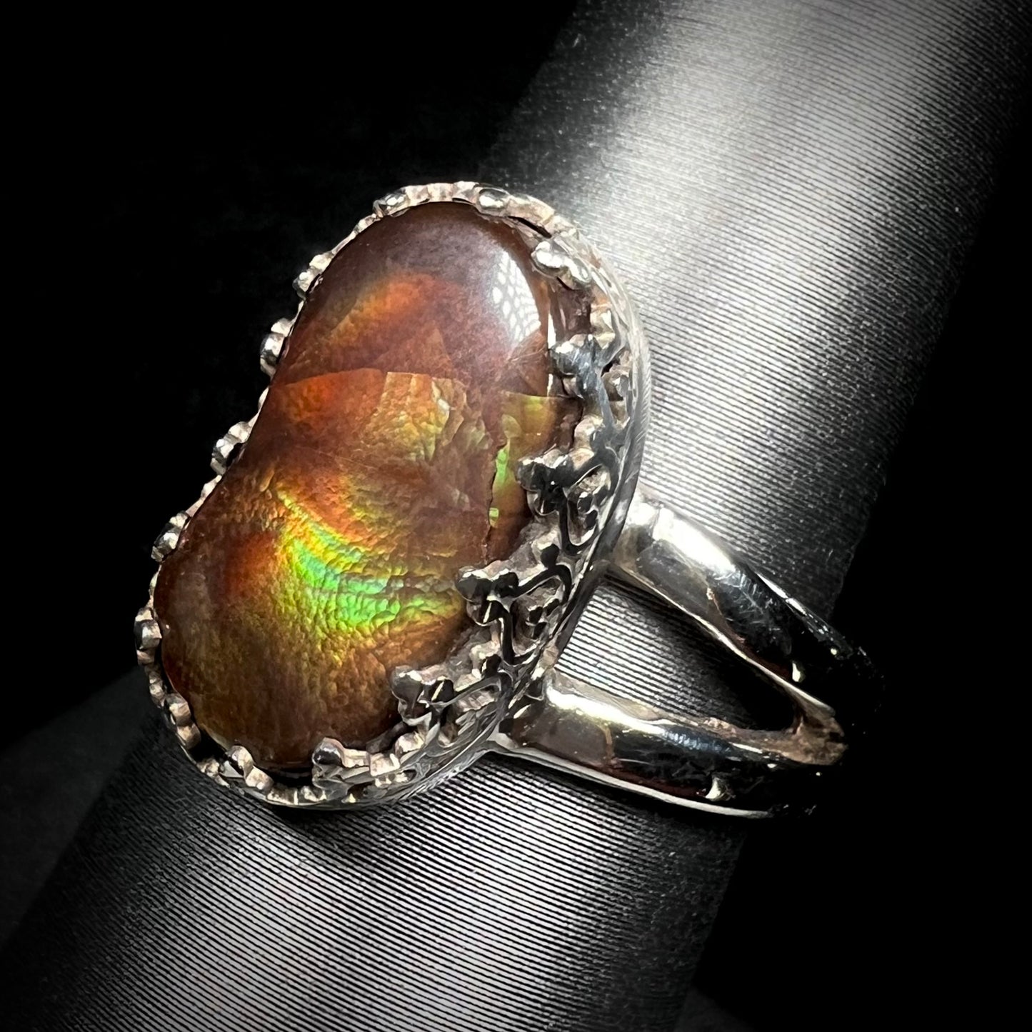 A fire agate ring with silver crown-design prongs shown at an angled view against black backdrop.