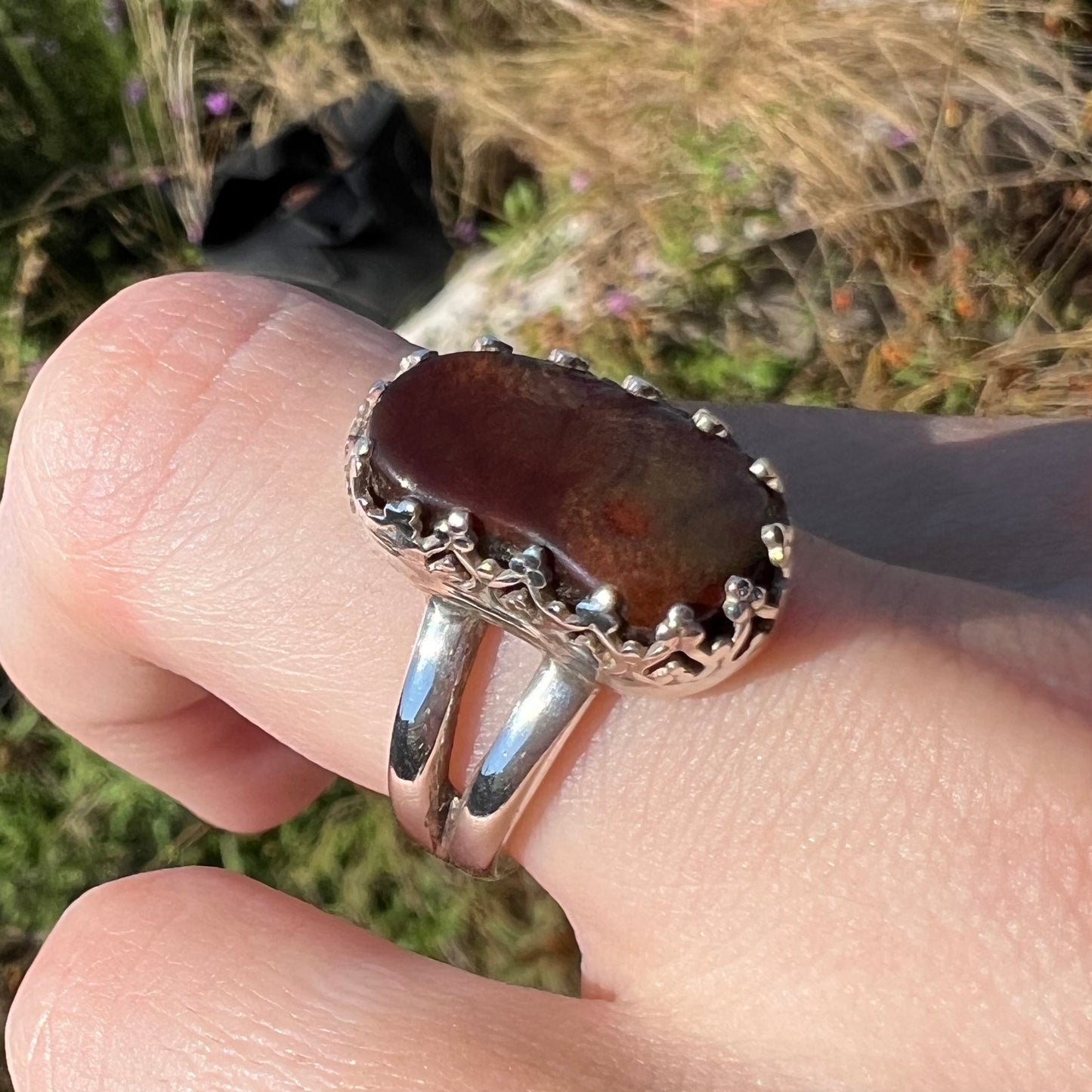 Silver crown-design fire agate ring worn on finger at an angle in the sun. The stone appears brown with no color.