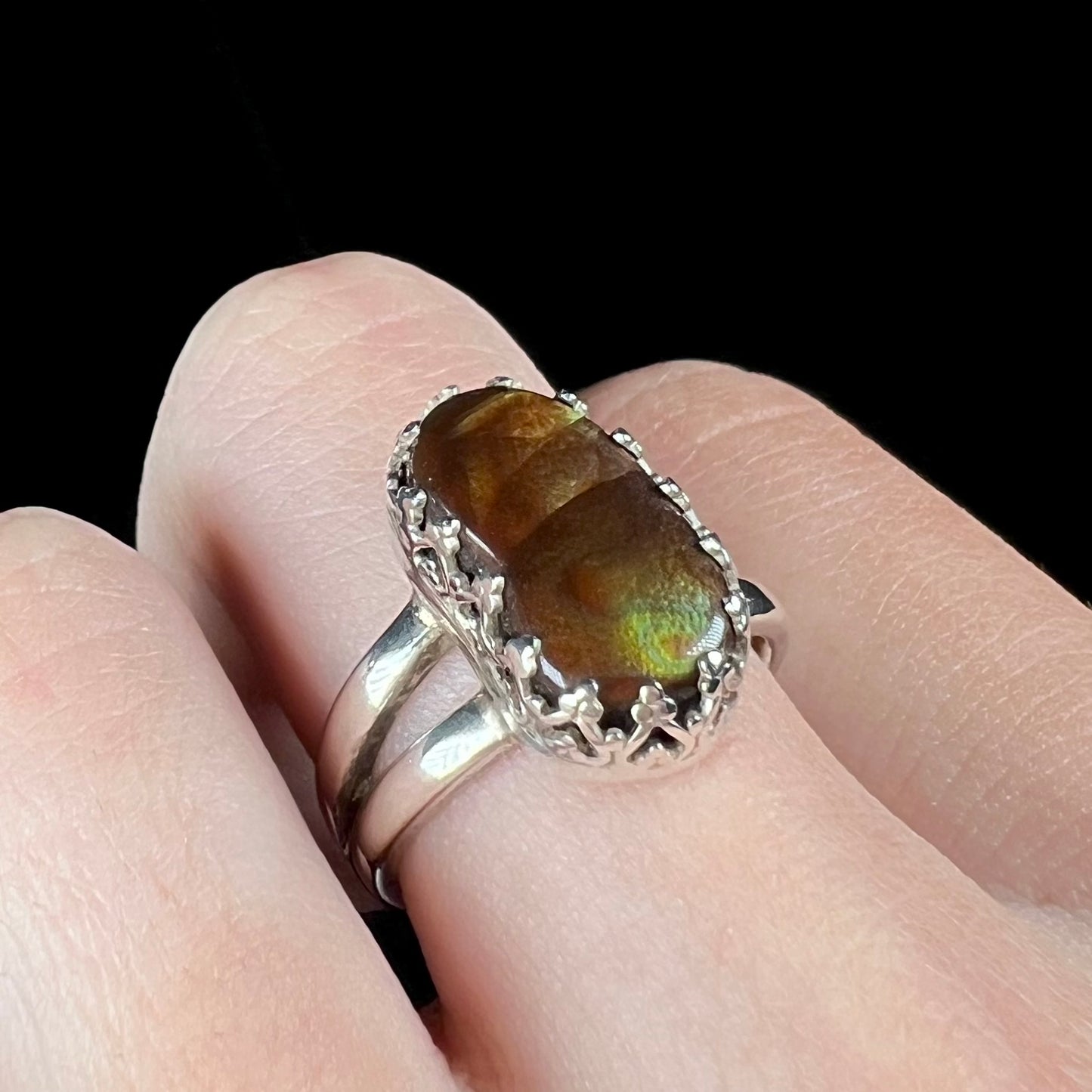 Finger wearing a crown-design silver fire agate ring, shown at an angle against black backdrop.