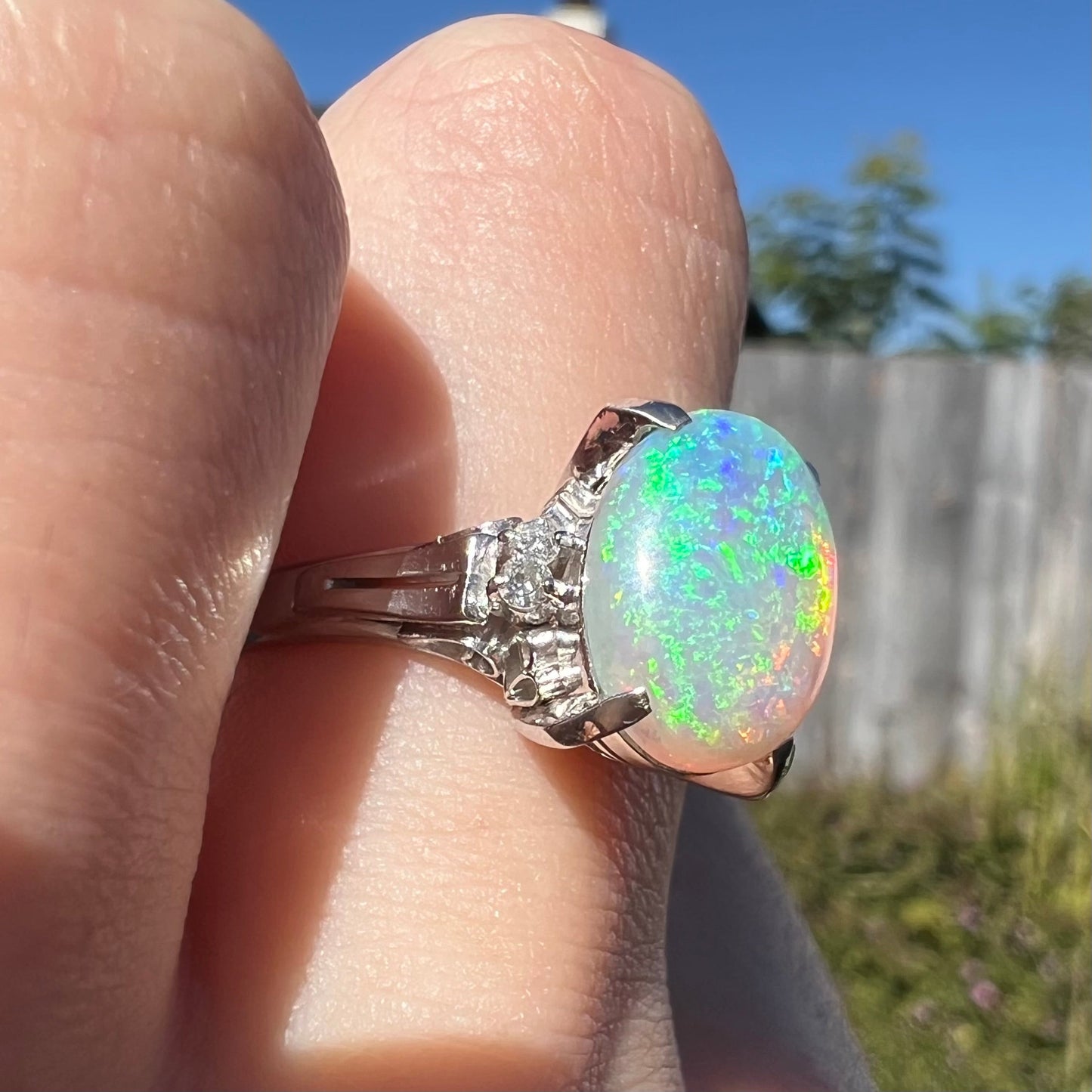 A platinum filigree opal engagement ring set with diamond accents. The opal has green-blue colors.