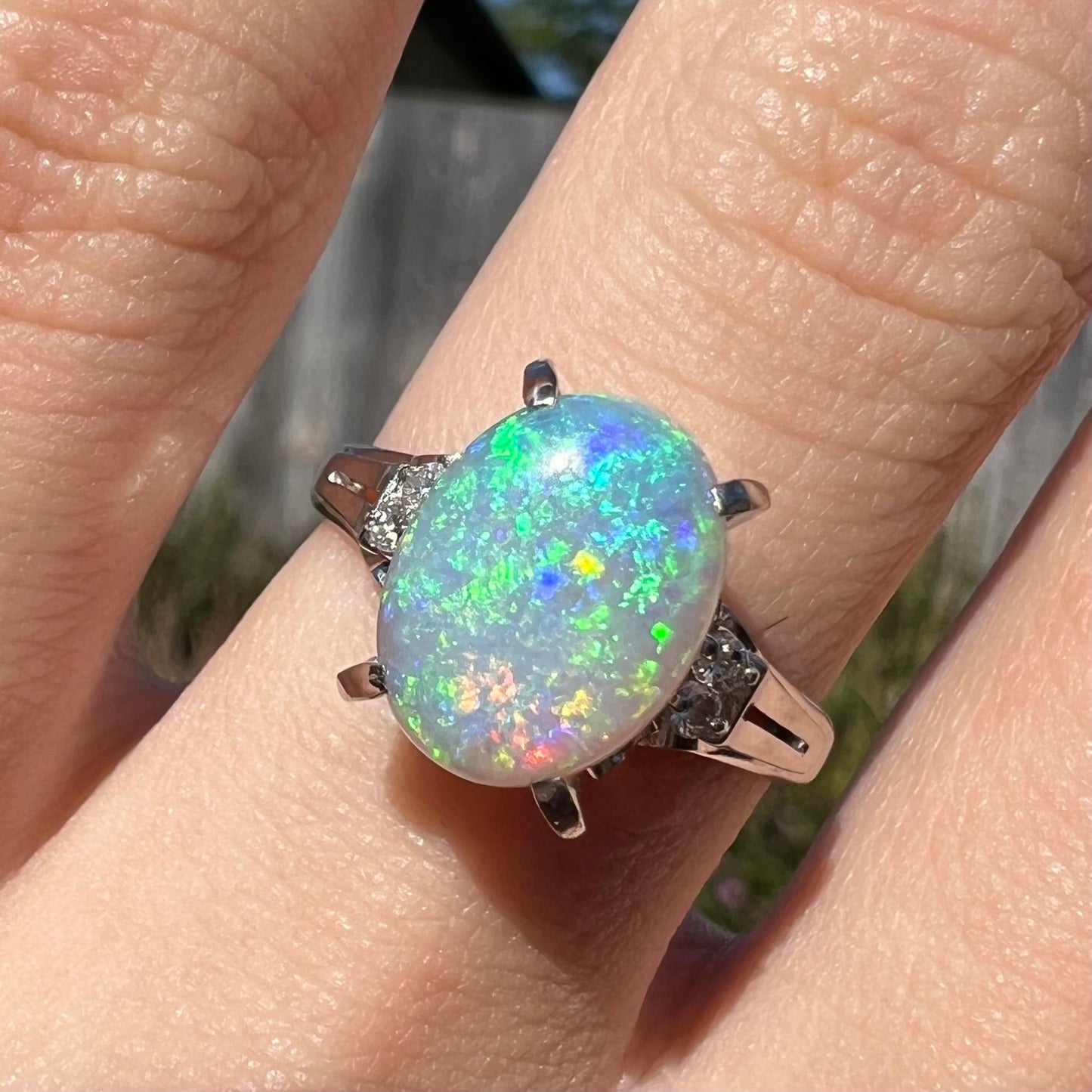 A platinum filigree opal engagement ring set with diamond accents. The opal has green-blue colors.
