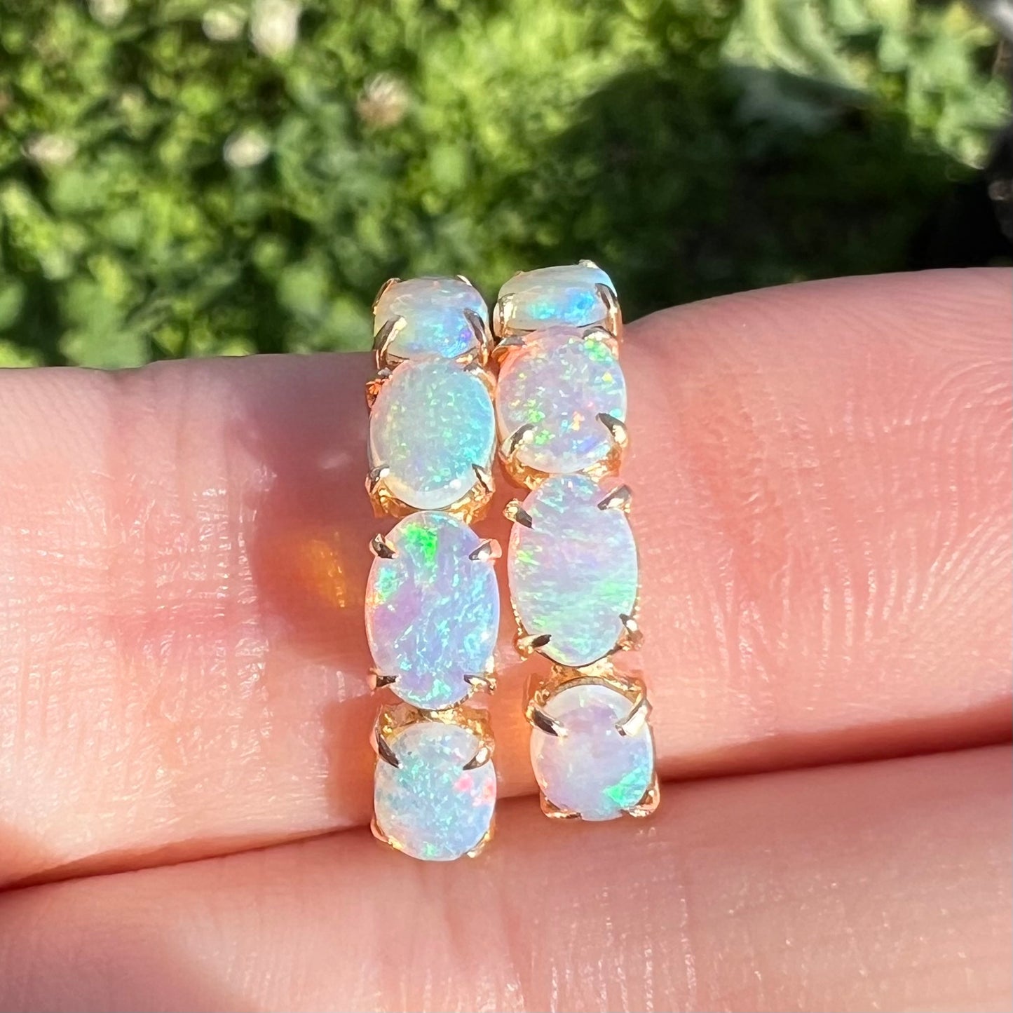 Macro straight-on view of opal hoop earrings in sunlight wrapped around a finger.