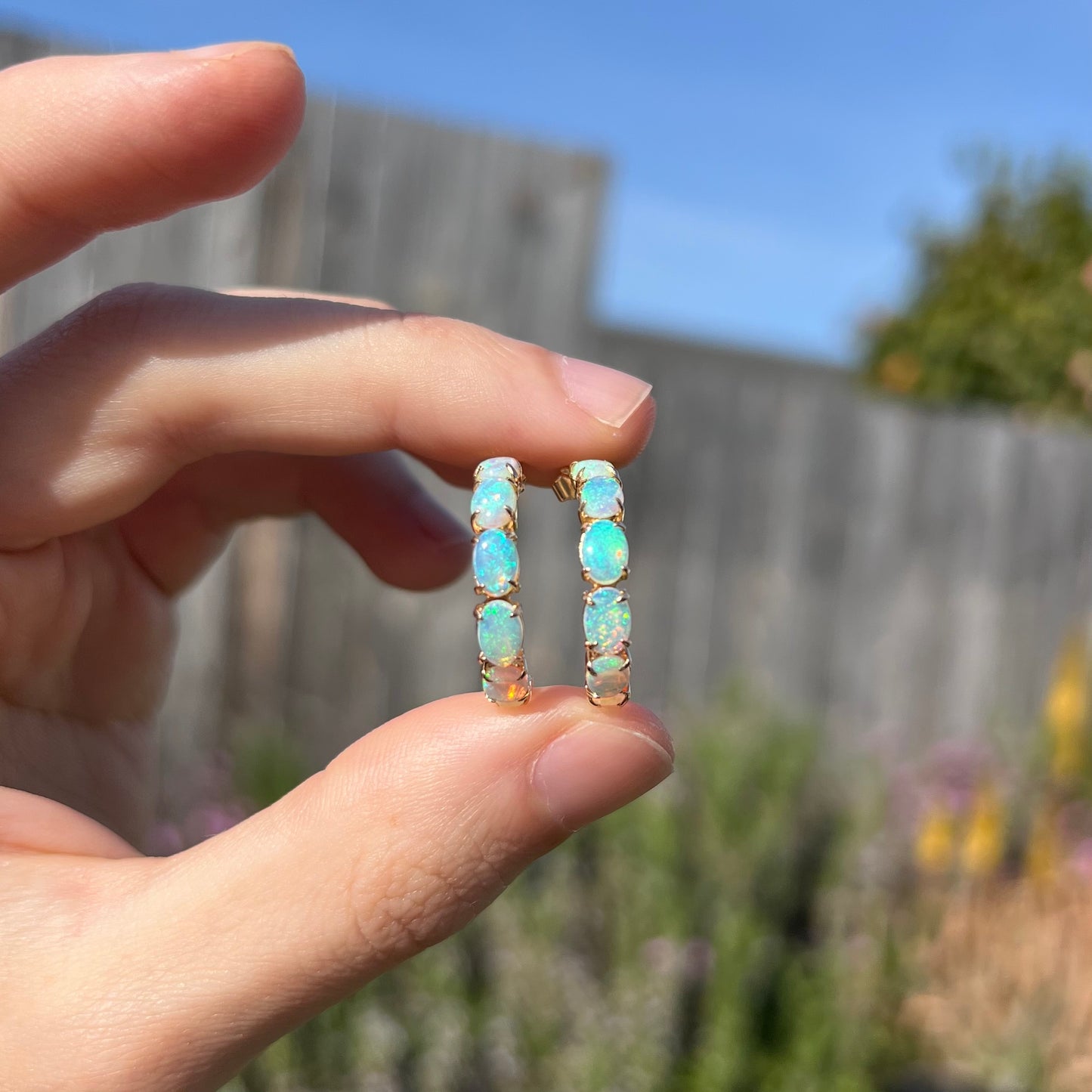 Opal hoop earrings shown outdoors in sunlight, revealing soft green and blue colors.