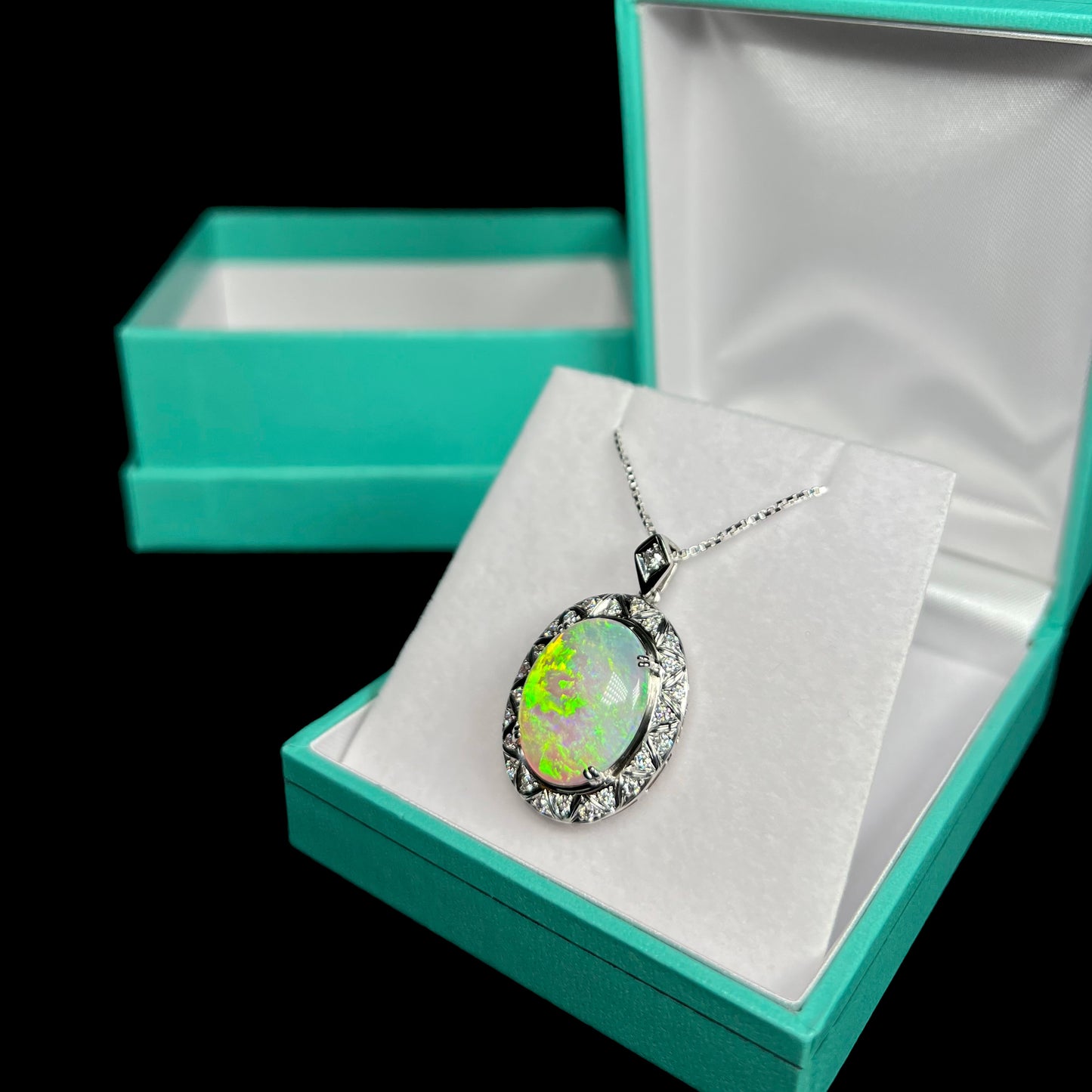 Diagonal shot of crystal opal pendant in box showing soft green and orange flashes.