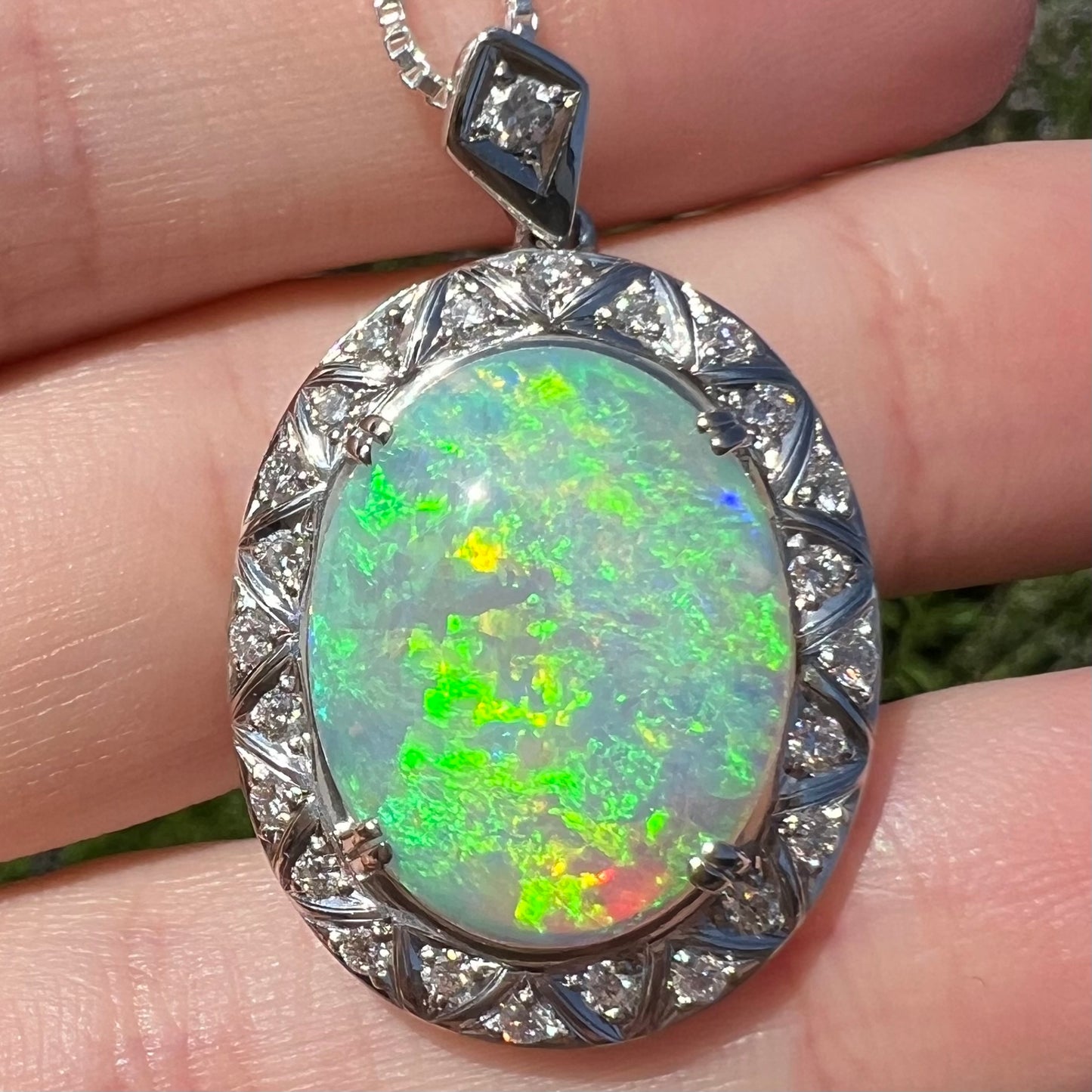 Macro close-up of opal pendant in sunlight showing intense green flash with red, blue, and yellow sparks.