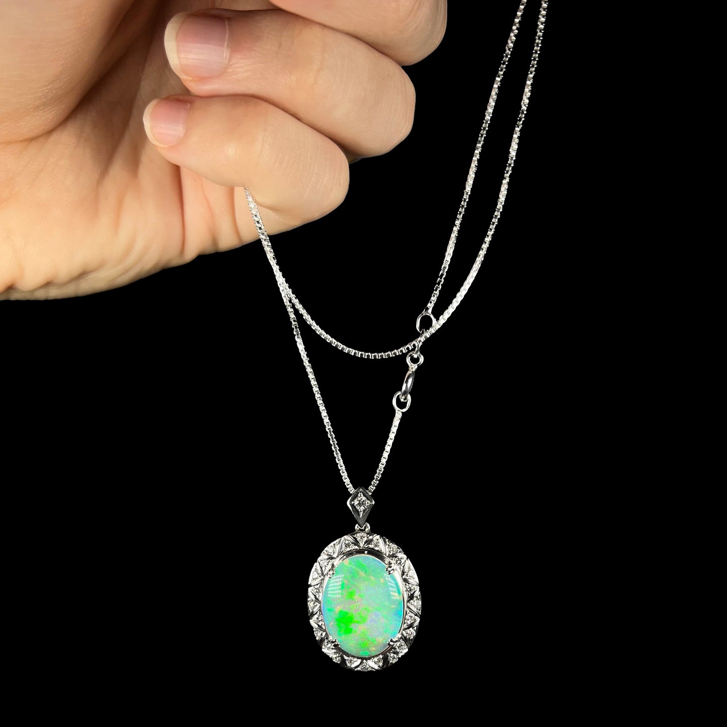 Crystal opal necklace with green flash, held by the chain against a black background.