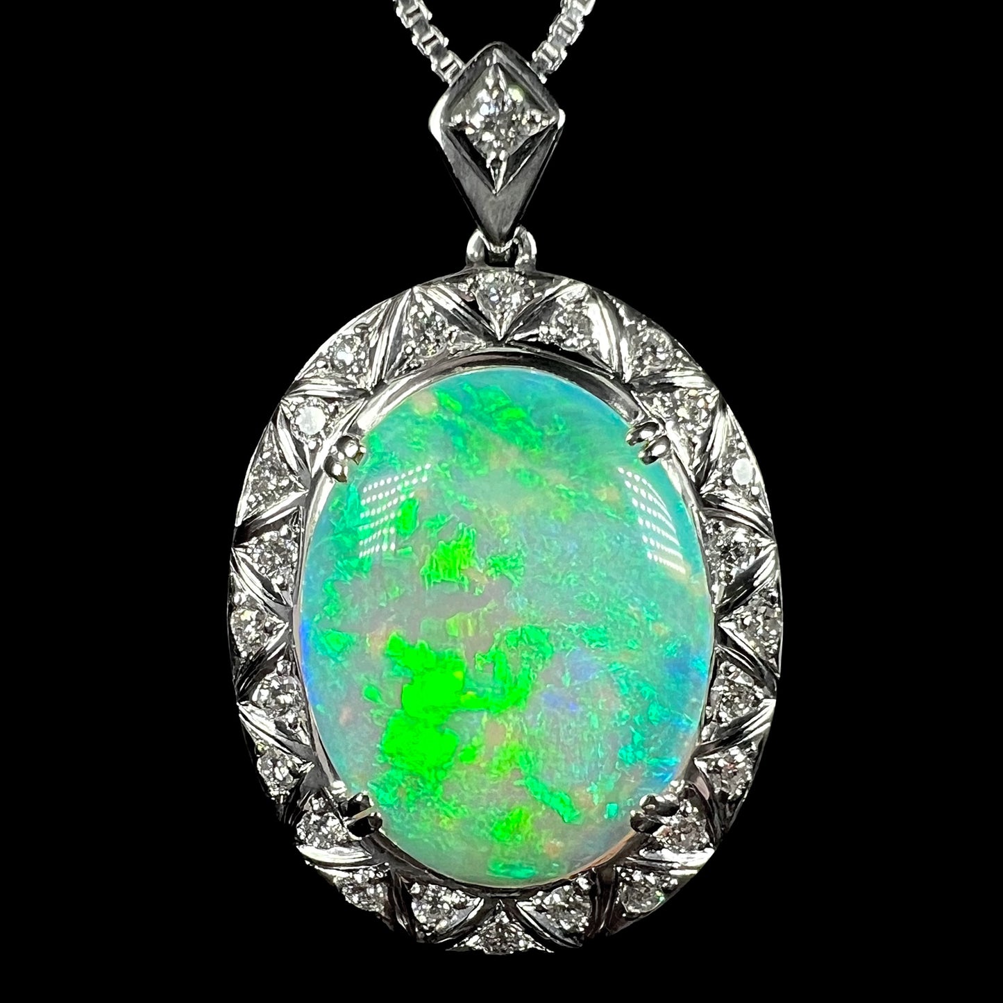 A platinum crystal opal pendant with a strong green flash, photographed close-up against a black background.