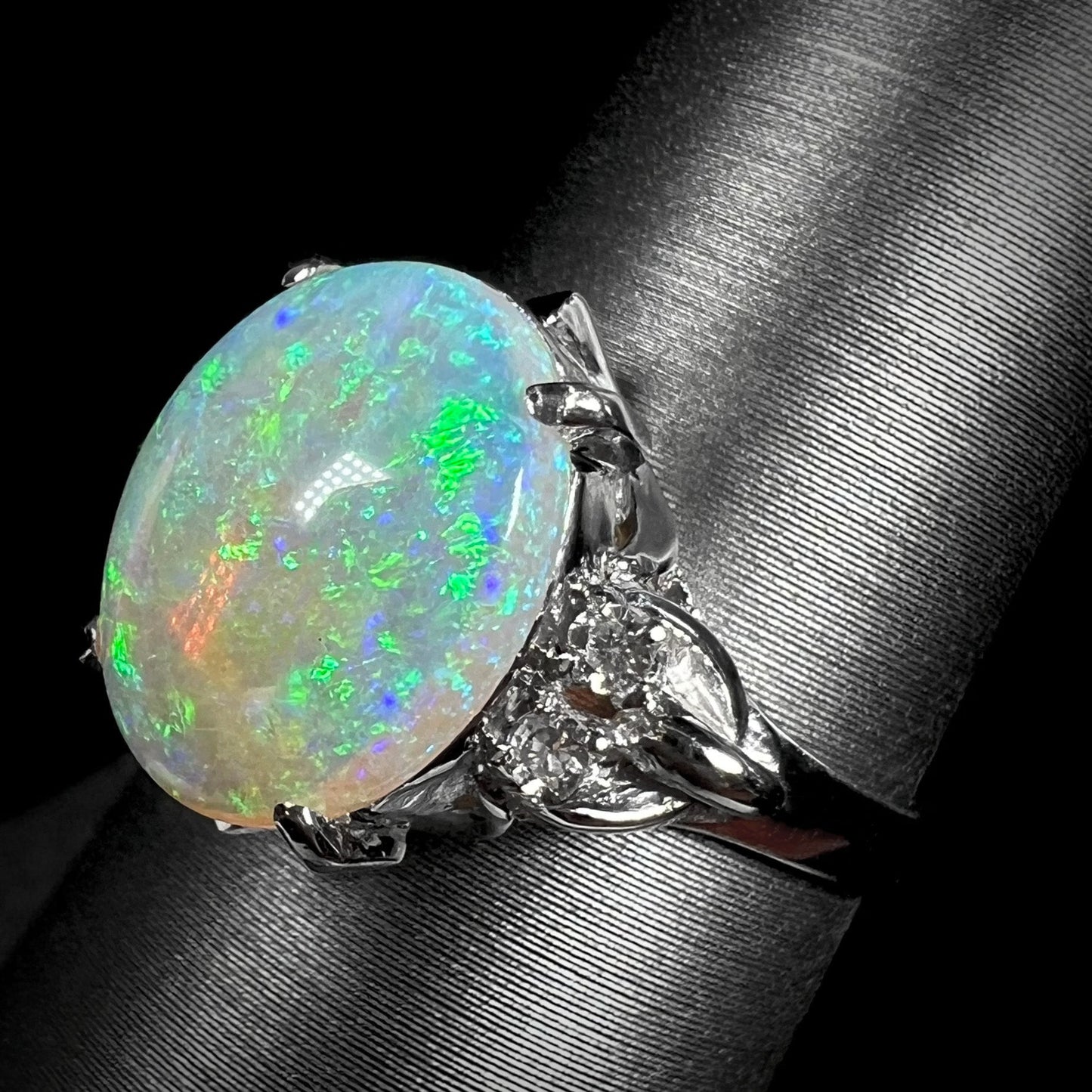 An Australian crystal opal and diamond engagement ring set in a platinum filigree mounting. The opal plays green/blue colors and has a crack.