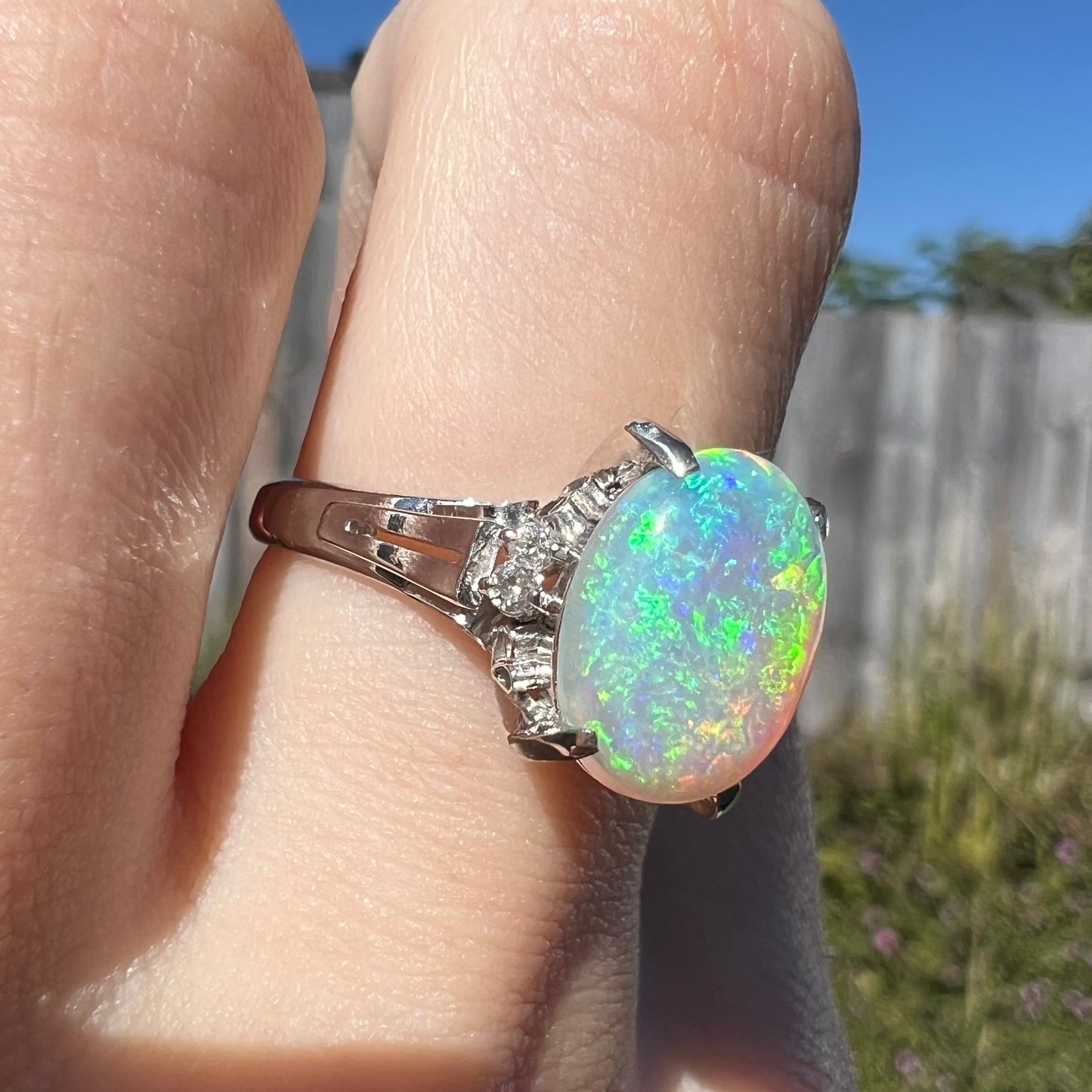 A platinum filigree opal engagement ring set with diamond accents. The opal has green-blue colors.