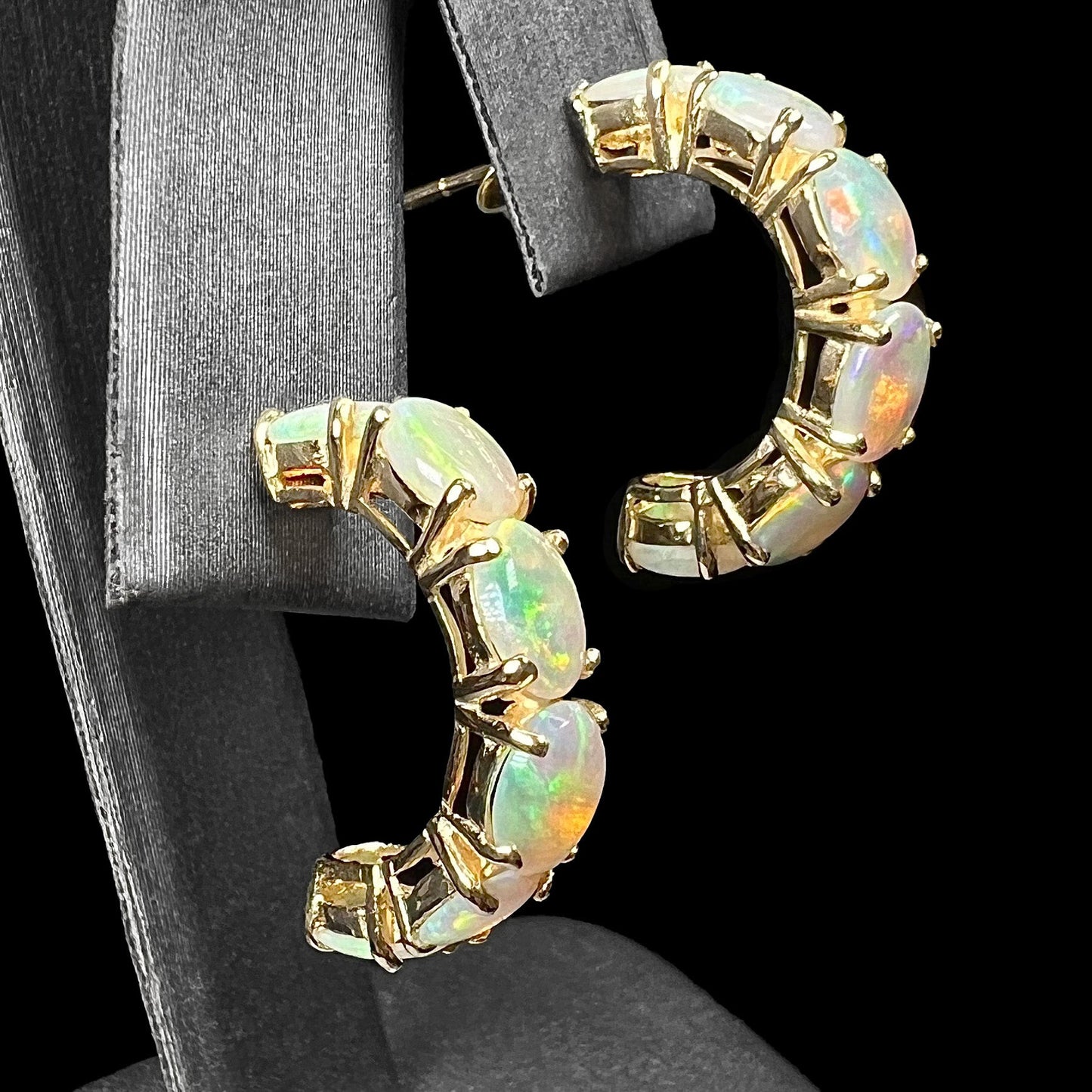 A pair of yellow gold opal hoop earrings. Each earring is set with six natural oval cut opals.