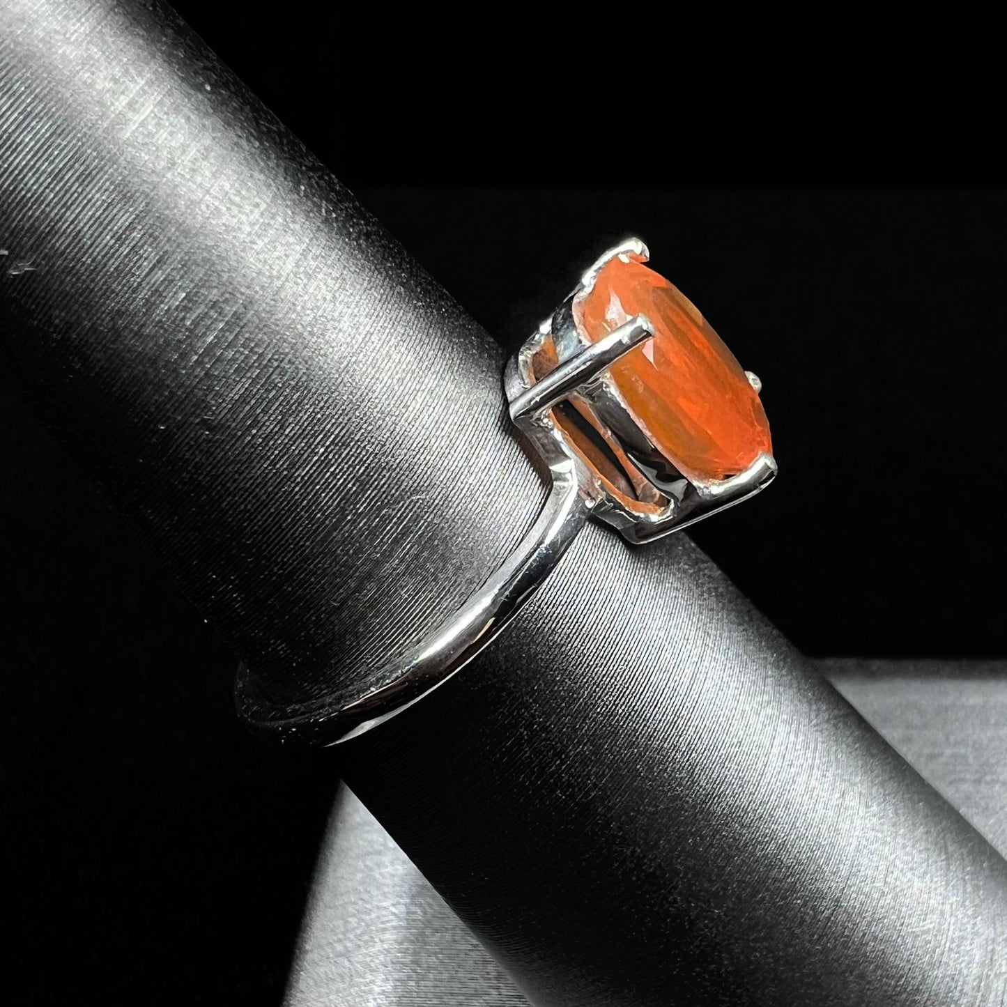 A silver solitaire ring set with a natural, faceted oval cut Mexican fire opal. The stone is a bright orange color.