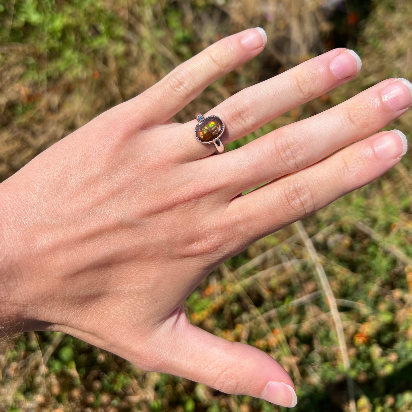A dainty fire agate ring for ladies worn on a hand in sunlight. The fire agate shines green colors.