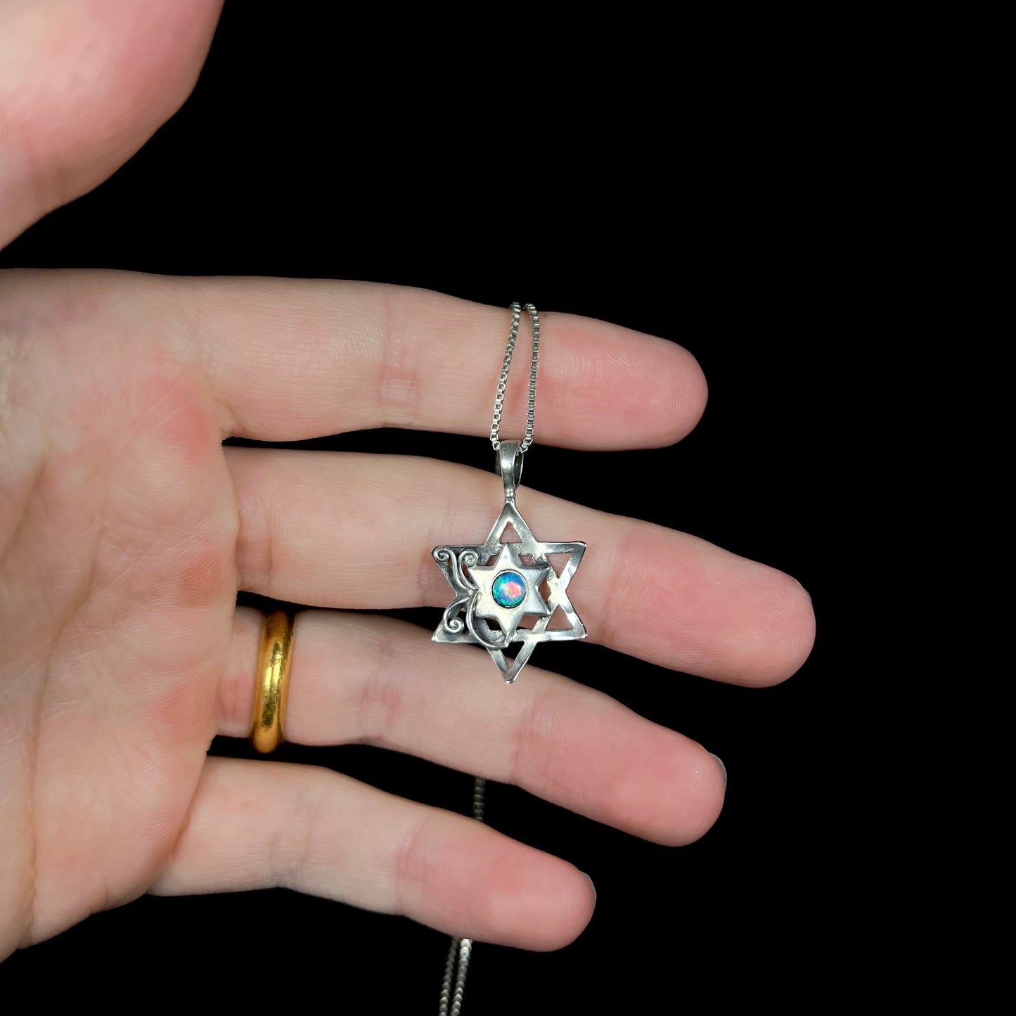 A dainty opal Star of David necklace held in a hand against a black background.