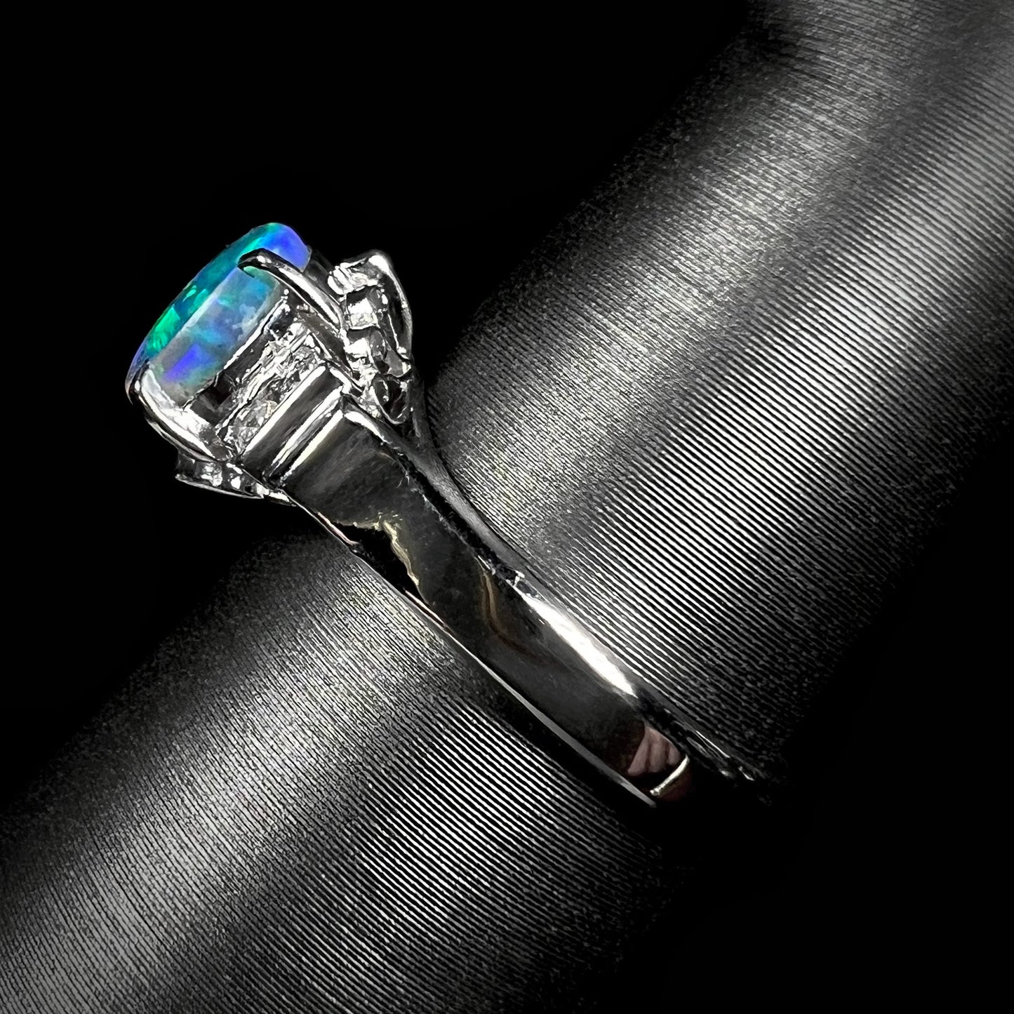 A dainty platinum black opal engagement ring, showcasing its elegant shank with delicate filigree details and sparkling diamond accents.