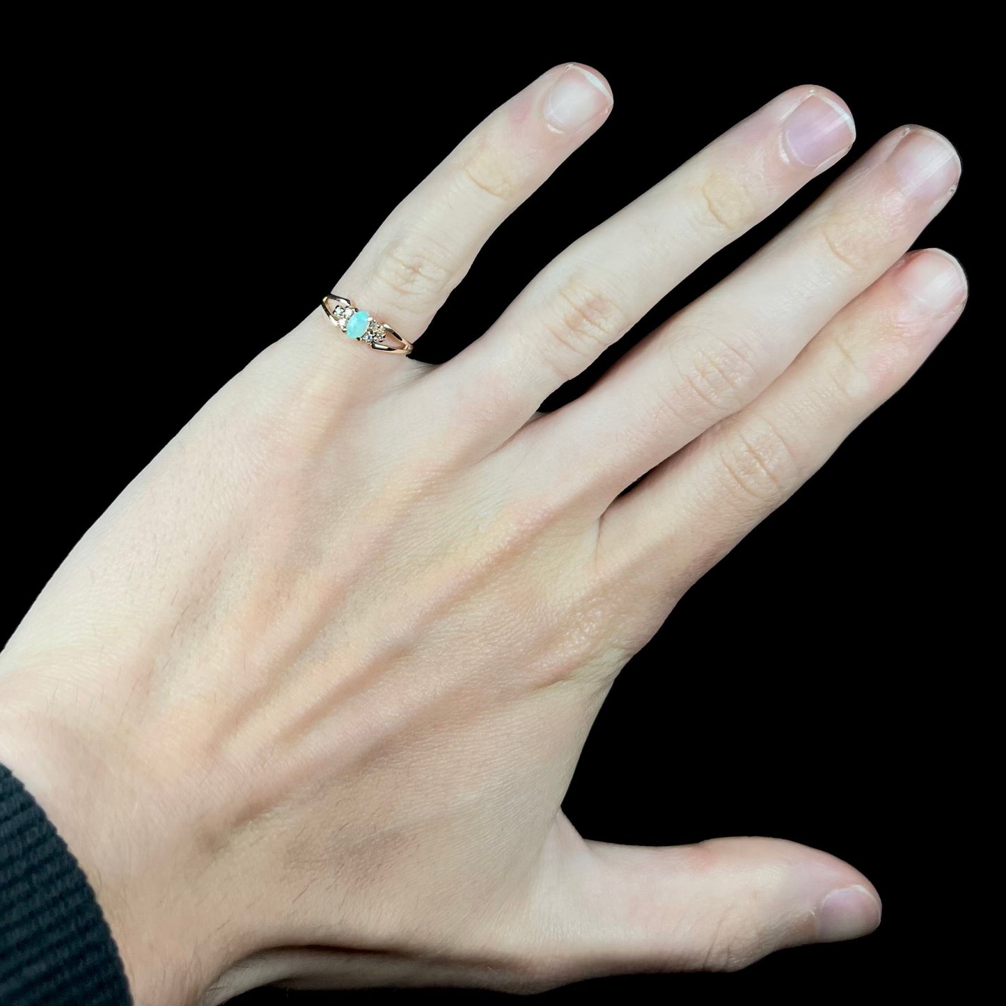 A ladies' yellow gold opal and diamond pinkie ring. The ring is a small size, and the opal shines green and blue colors.