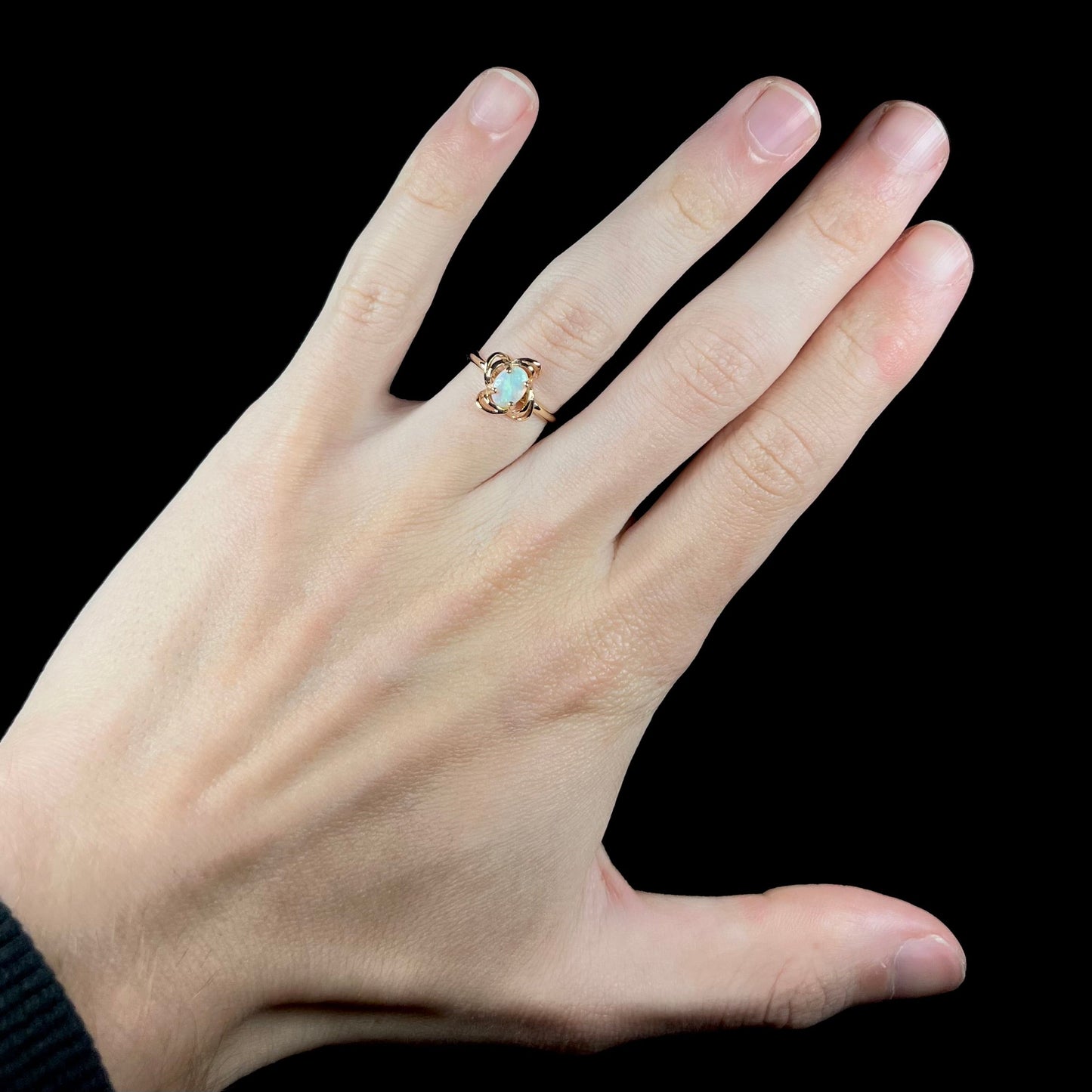A yellow gold ring mounted with an oval cut opal. The opal has a white base tone with green and blue color play.