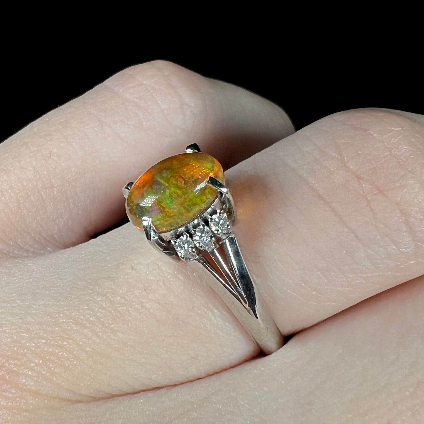 A platinum filigree and diamond-accented Mexican fire opal ring. The opal is orange with green fire.