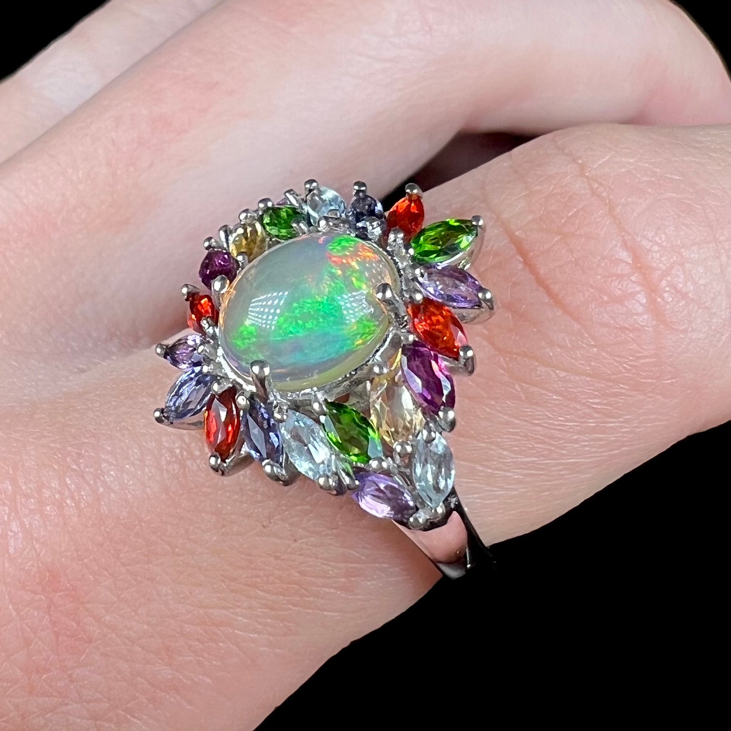 A D'Joy brand Ethiopian opal and gemstone ring, worn on a finger and shown at an angle.