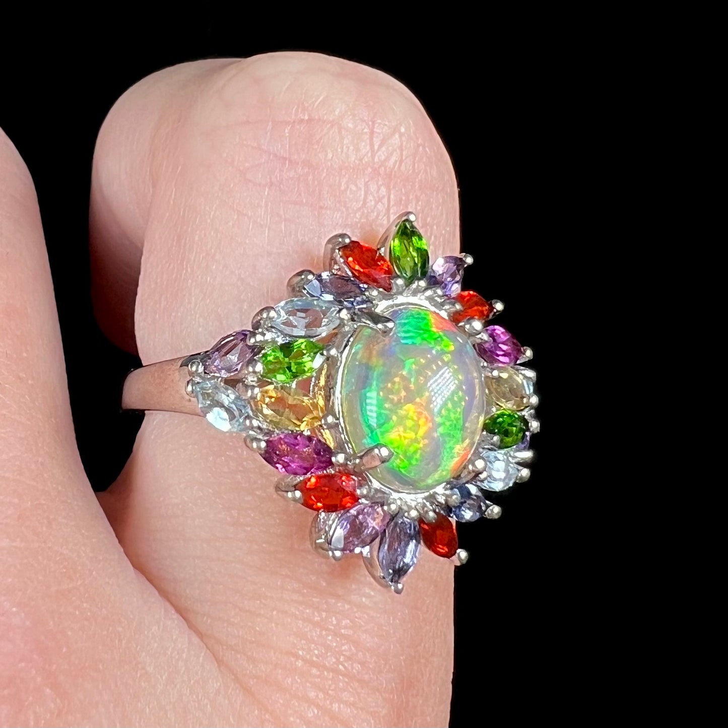 A rainbow Ethiopian opal and gemstone ring made by D'Joy, worn on a finger in LED light.