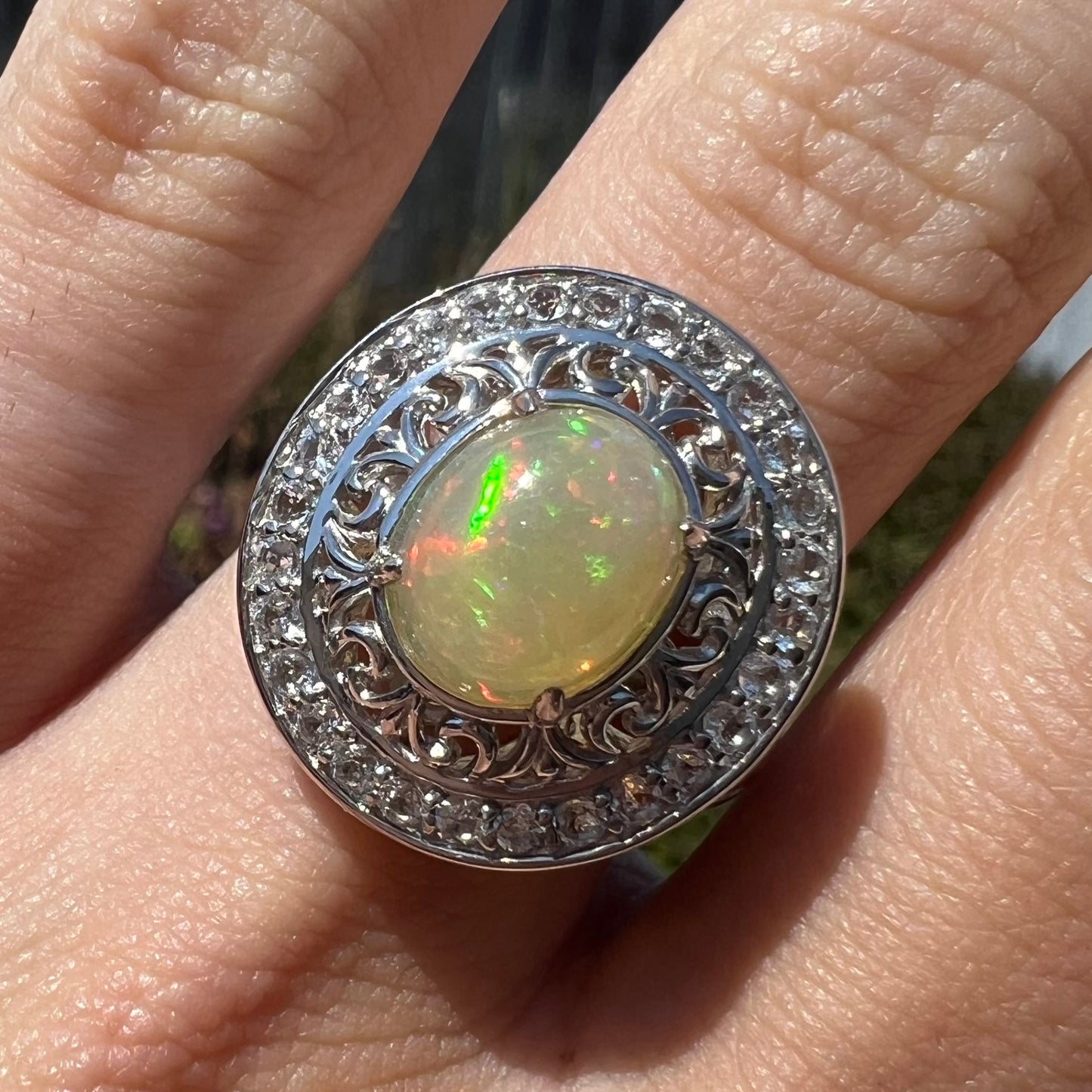 Close-up of finger wearing a double halo opal ring in natural sunlight.