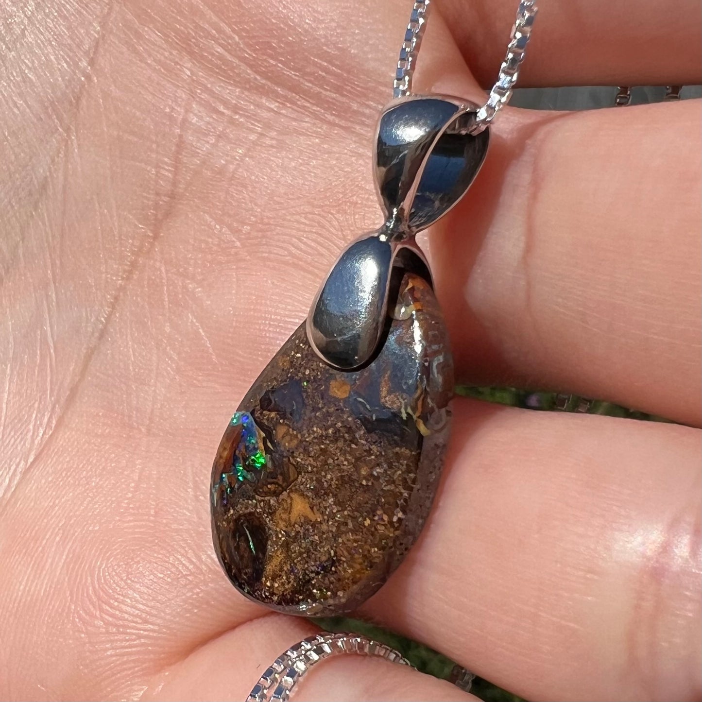 An Australian boulder opal necklace with a sterling silver bail. The opal has a bright green flash of color.