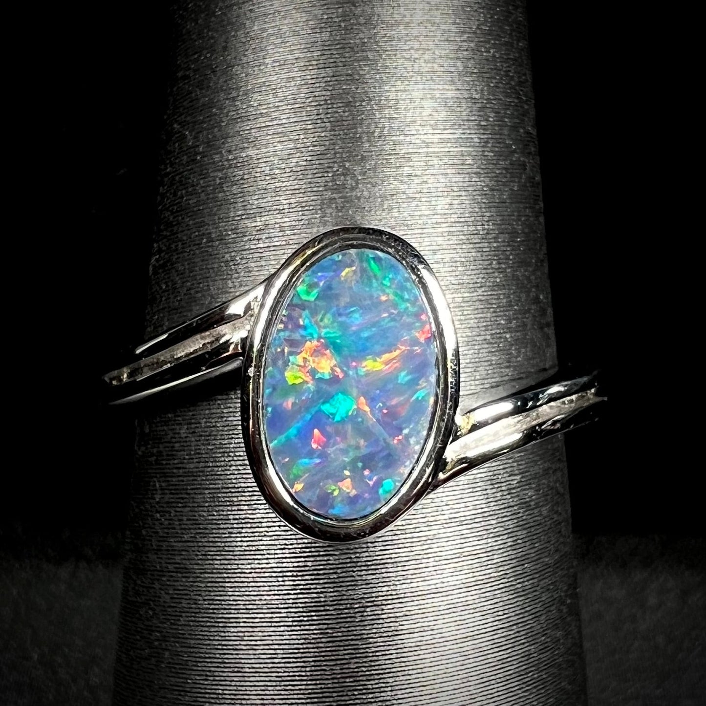 A sterling silver ring bezel-set with an oval shaped black opal doublet. The opal has red and blue fire.