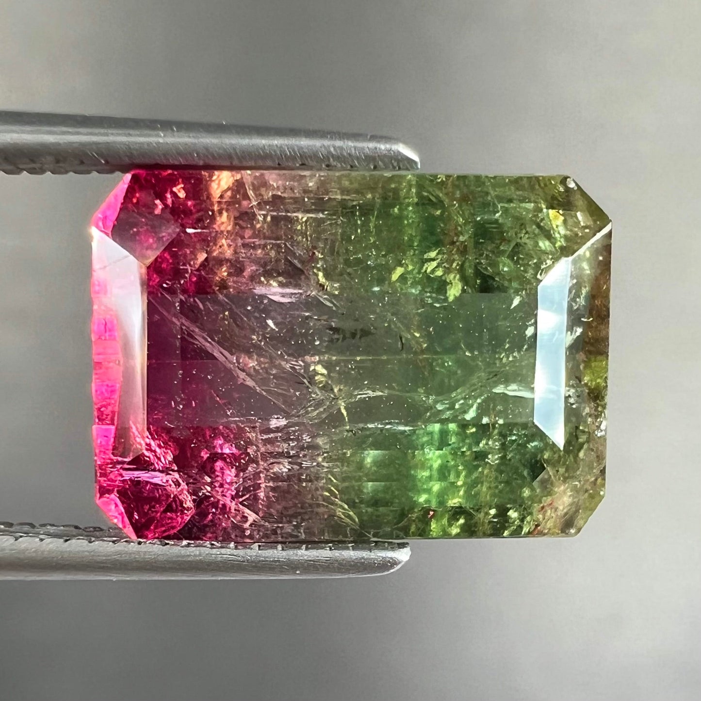 A loose watermelon tourmaline gemstone. The stone is emerald cut and fades from hot pink to green.