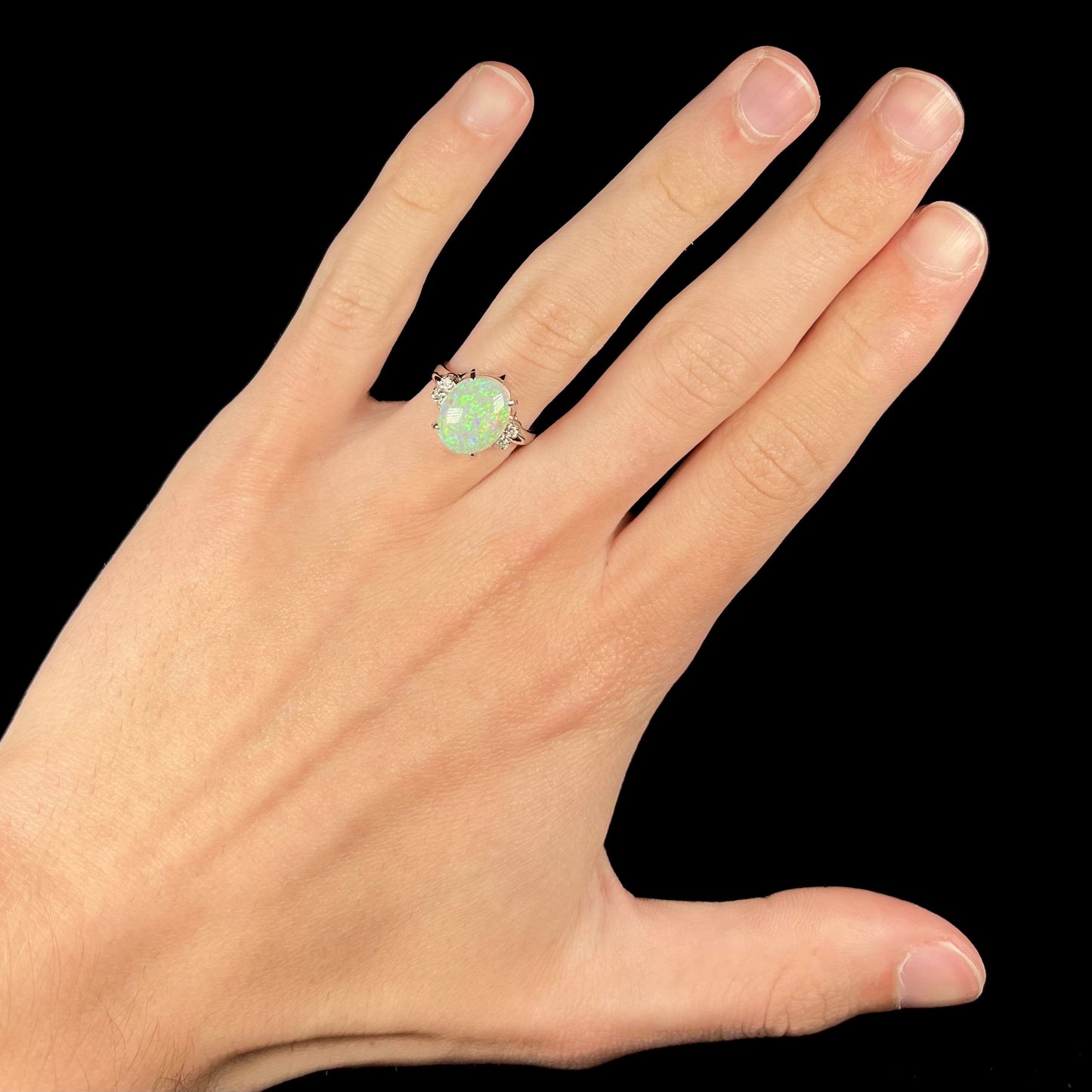 An Australian crystal opal and diamond engagement ring set in a platinum filigree mounting. The opal plays green/blue colors and has a crack.