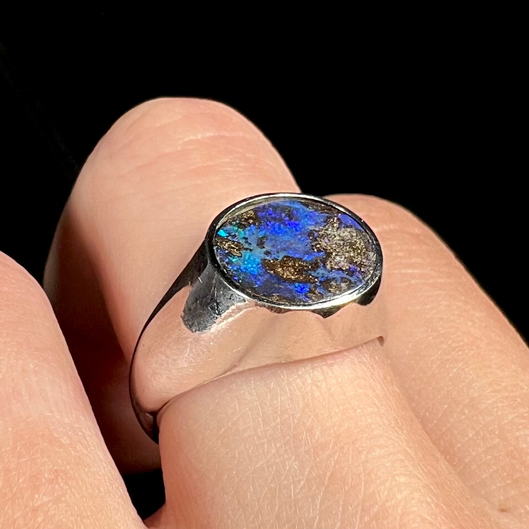 Angled close-up view of an estate men's Australian boulder opal ring with blue color play worn on a finger.