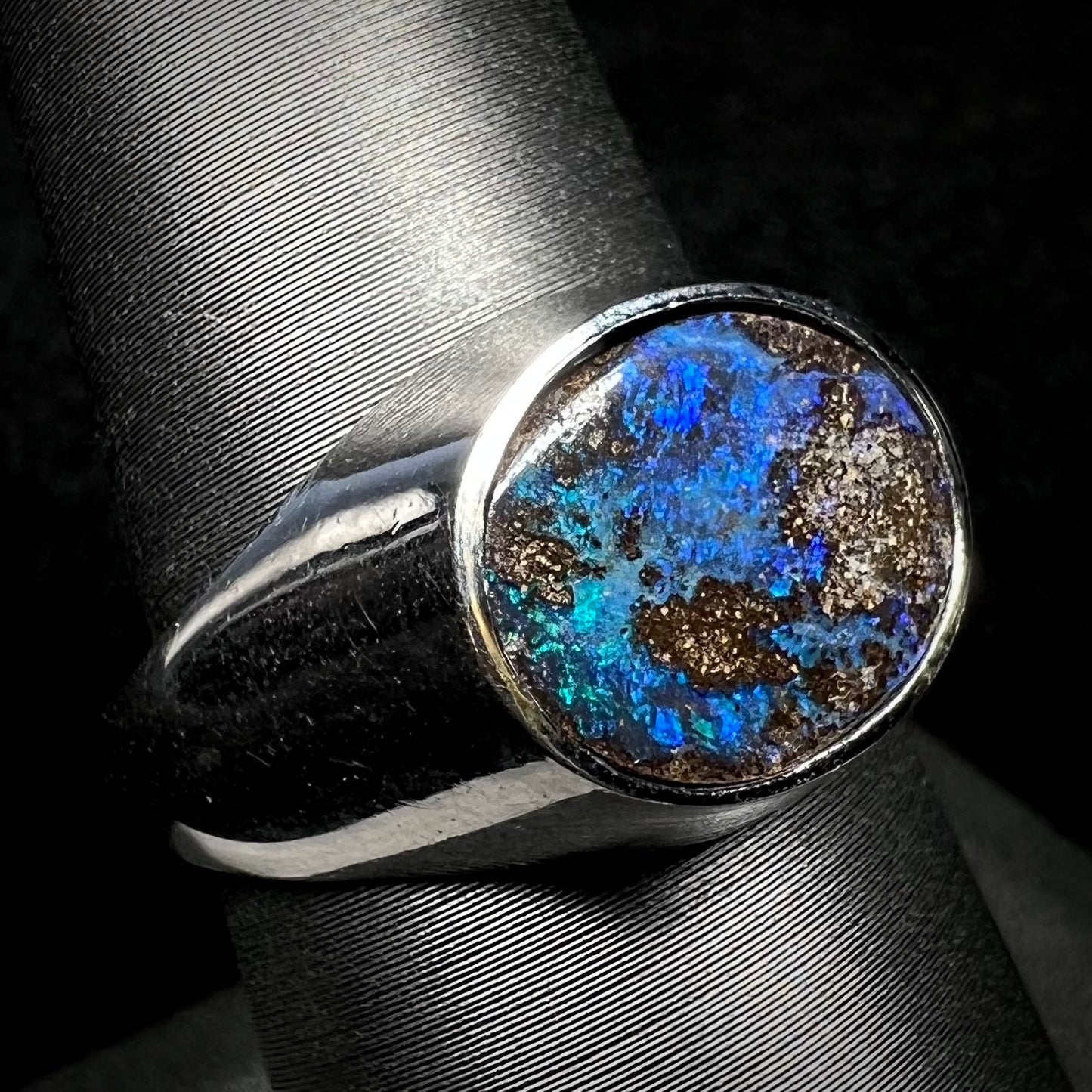 A stainless steel men's Australian boulder opal ring with blue color play, shown on a ring display from an angle.
