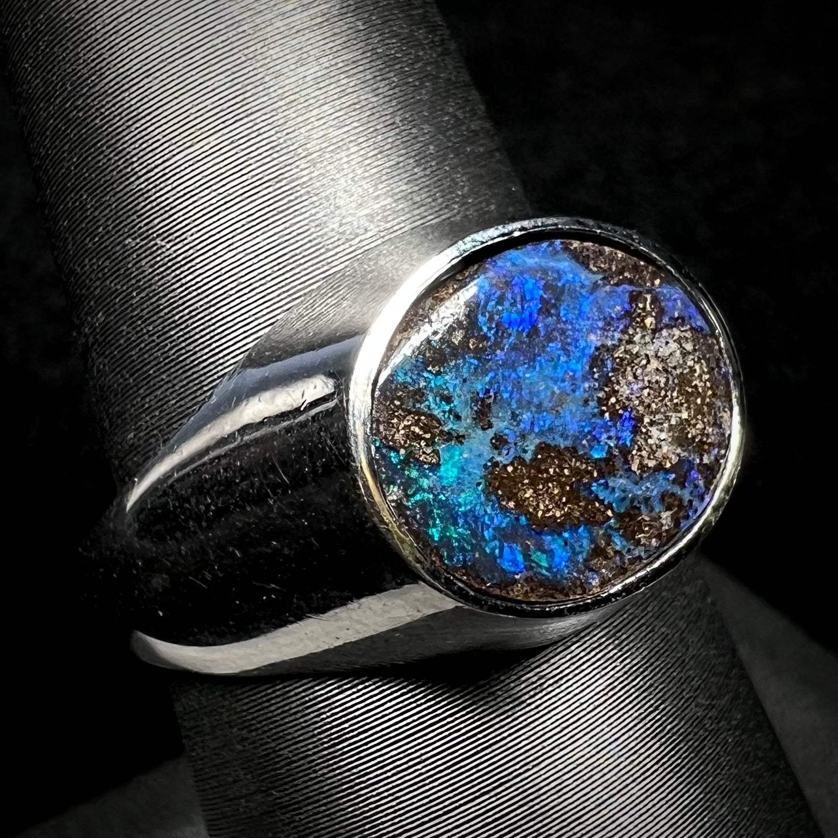 A stainless steel men's Australian boulder opal ring with blue color play, shown on a ring display from an angle.