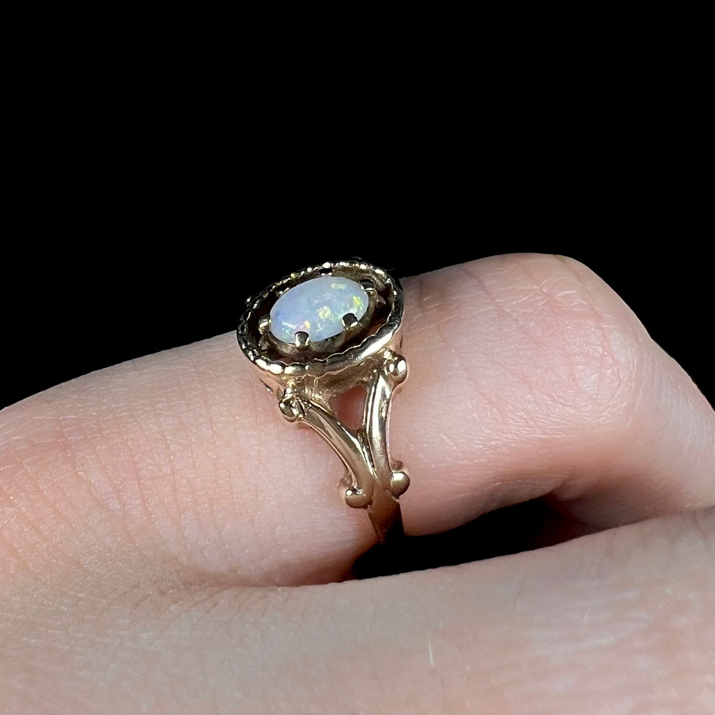 A ladies' Art Nouveau style opal solitaire ring. The mounting is yellow gold with filigree accents.