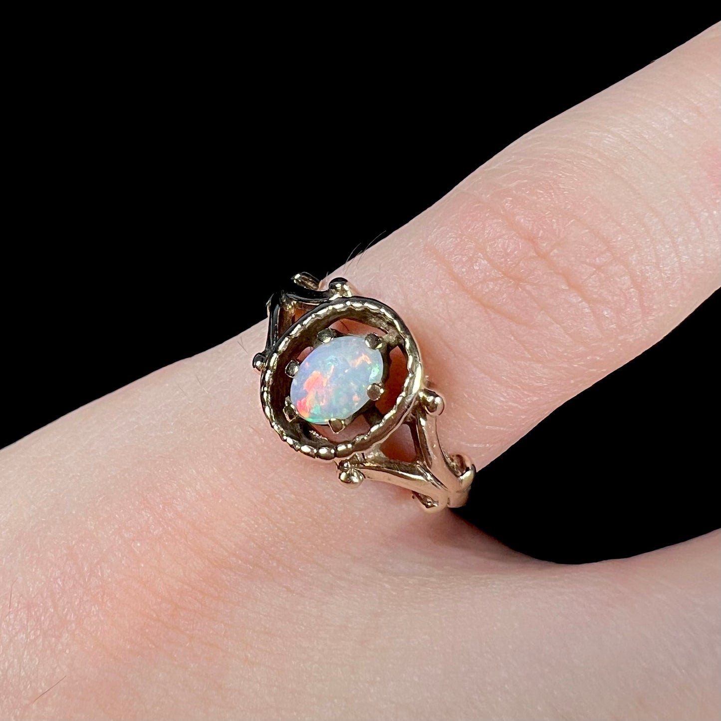 A ladies' Art Nouveau style opal solitaire ring. The mounting is yellow gold with filigree accents.