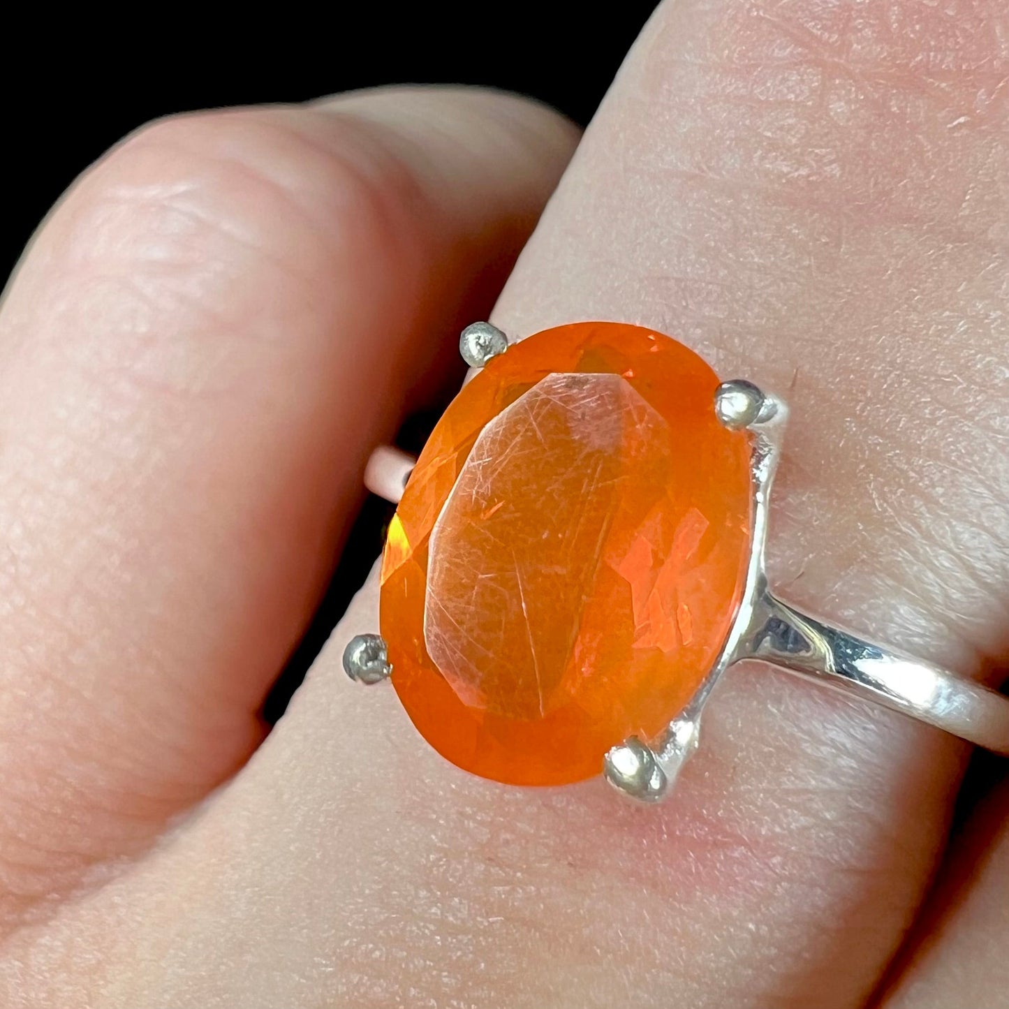 A silver solitaire ring set with a natural, faceted oval cut Mexican fire opal. The stone is a bright orange color.