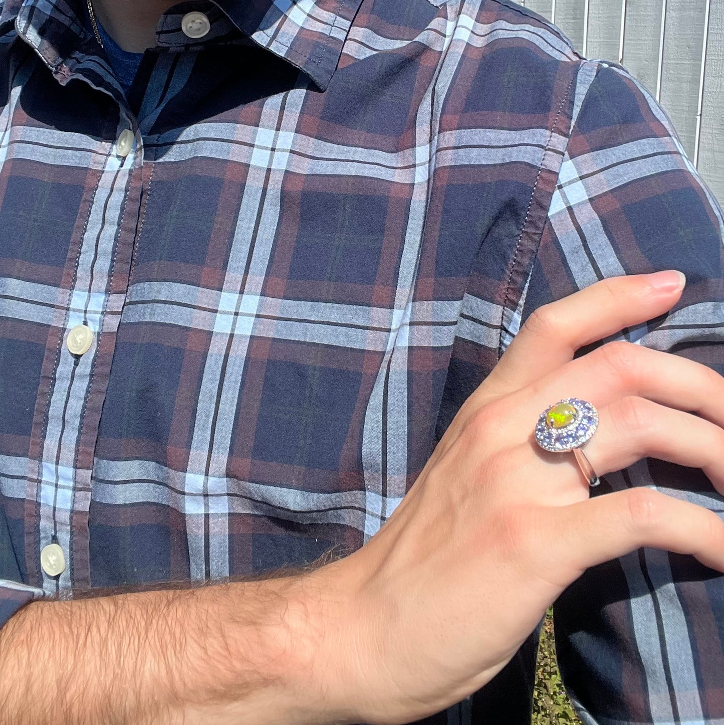 Person wearing a plaid shirt with a hand on shoulder wearing a ring featuring an Ethiopian opal and tanzanite ring.