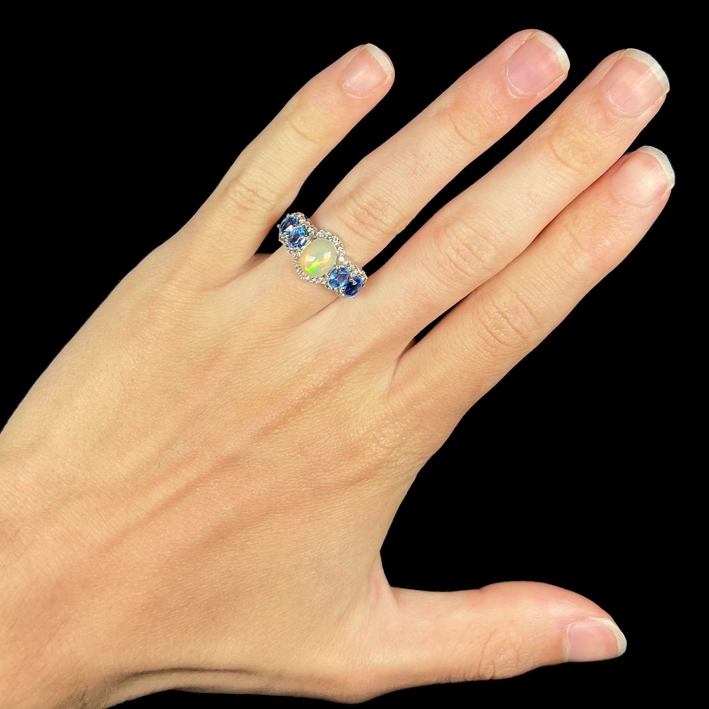 An Ethiopian opal and blue kyanite gemstone ring worn on a hand against a black background.