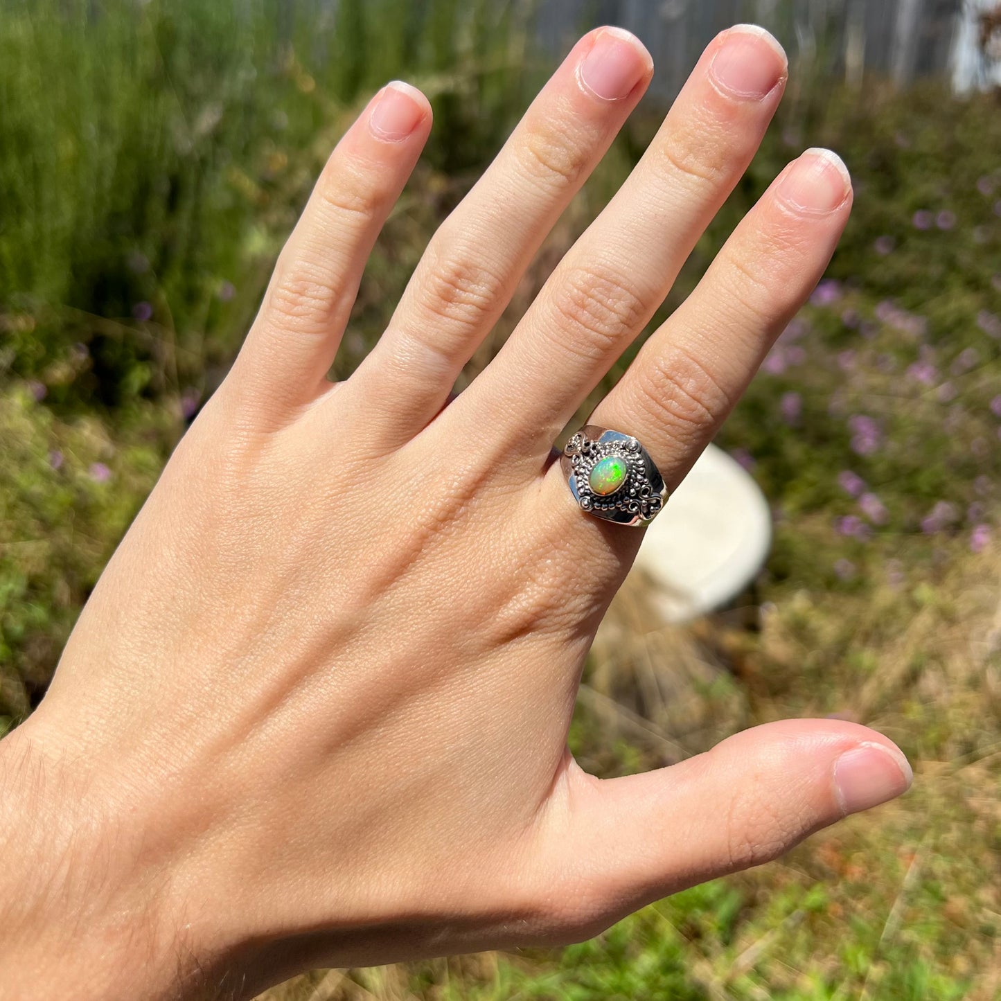 A Boho-style Ethiopian opal ring made from sterling silver, worn on the index finger of a hand in the sunlight.