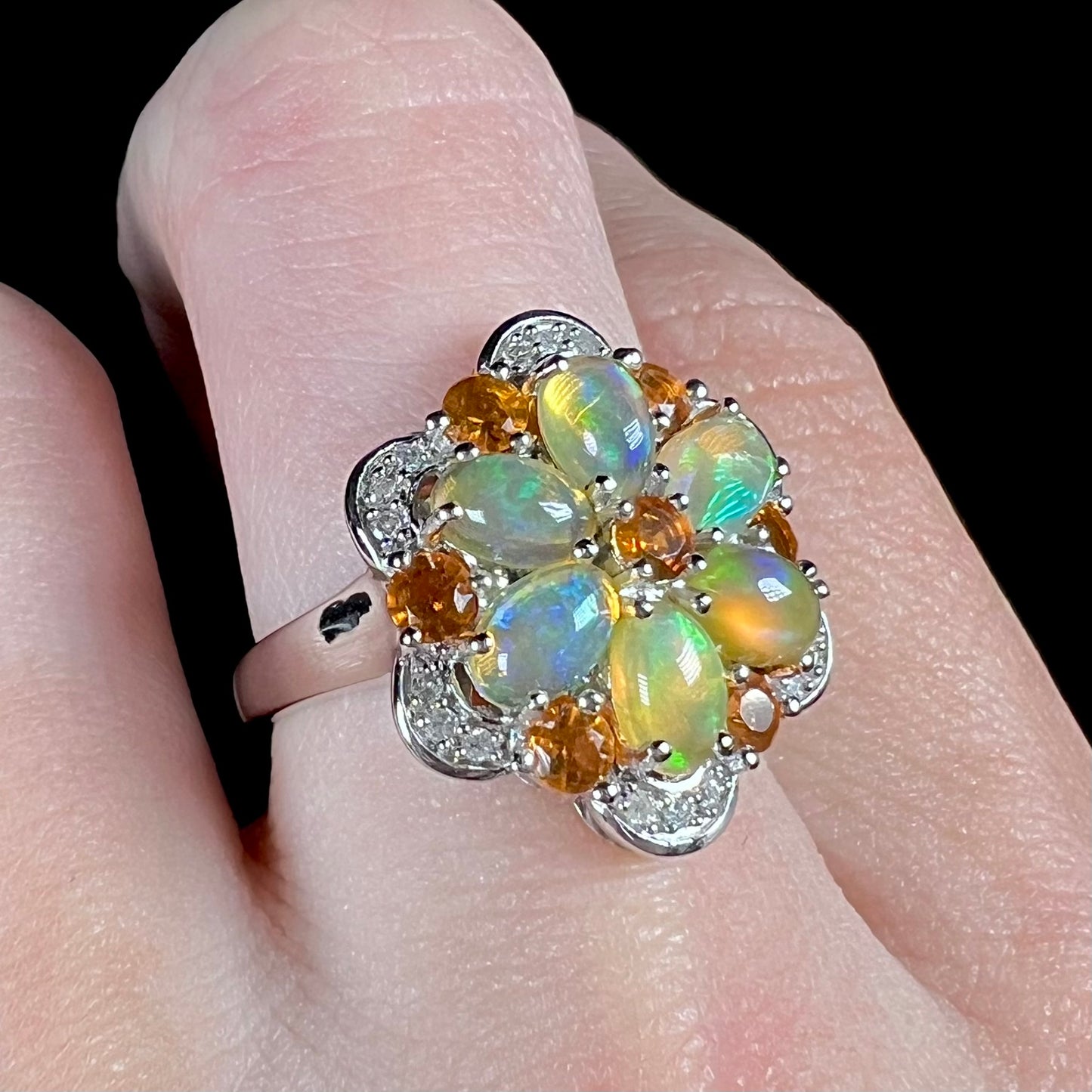 Angled view of an Ethiopian opal cluster ring resembling a flower worn on a finger against a black background.