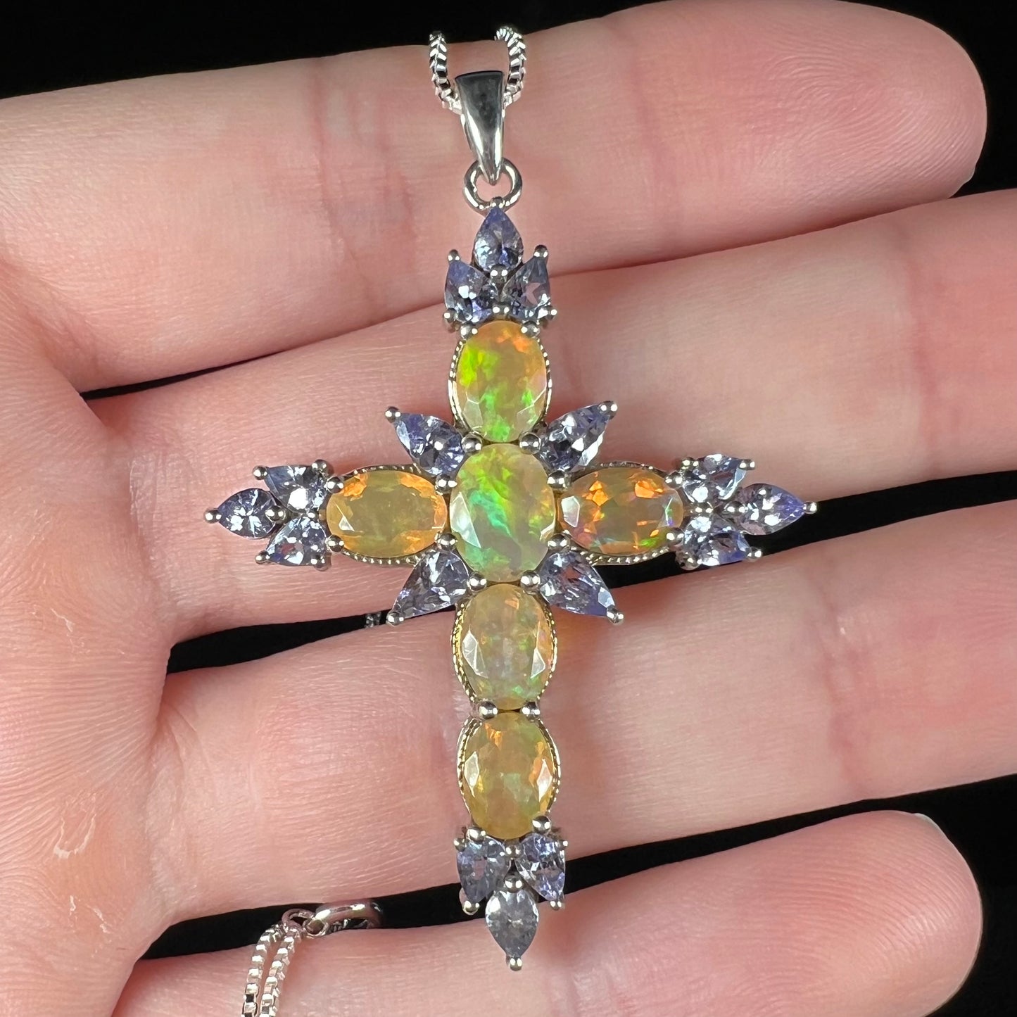An Ethiopian opal and tananite cross pendant made from sterling silver, held in a hand showing the front.