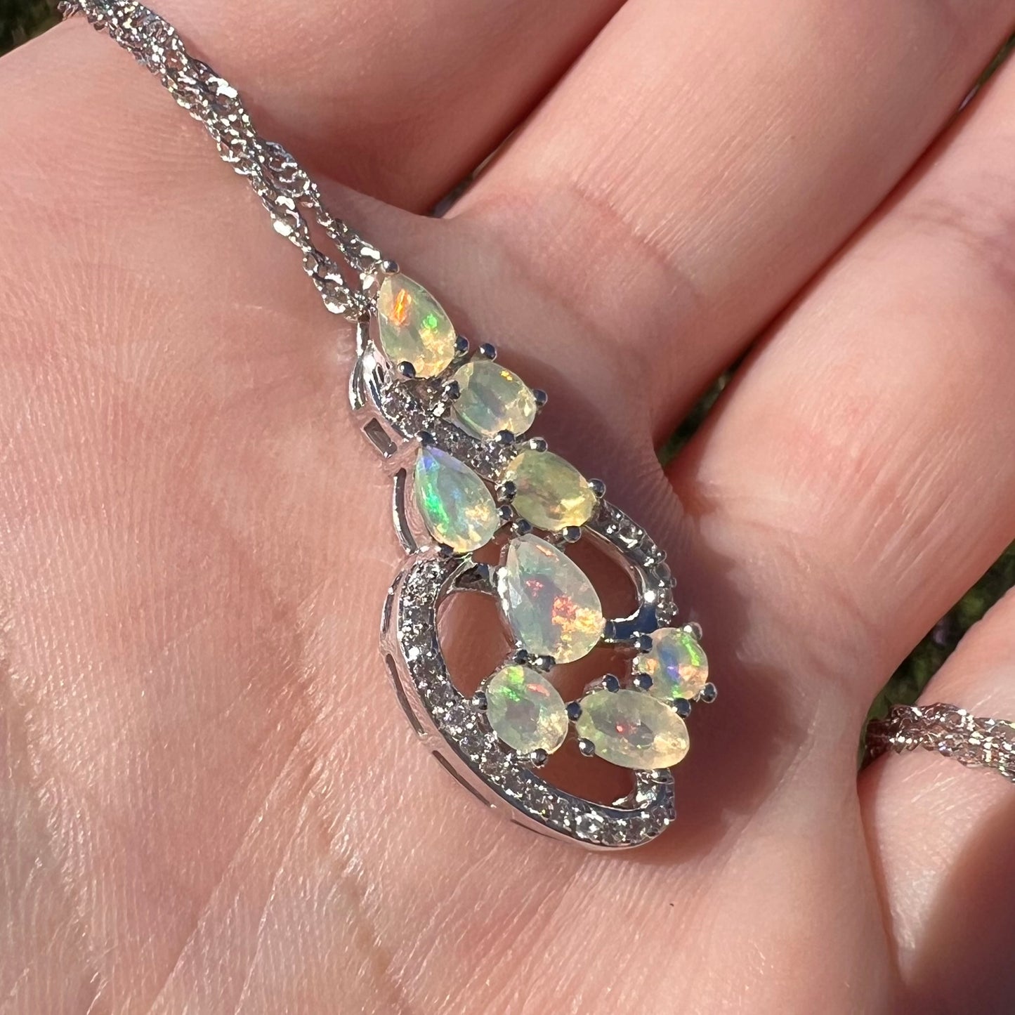 Angled close-up view of an Ethiopian opal and CZ necklace, held in a hand and shown in sunlight.