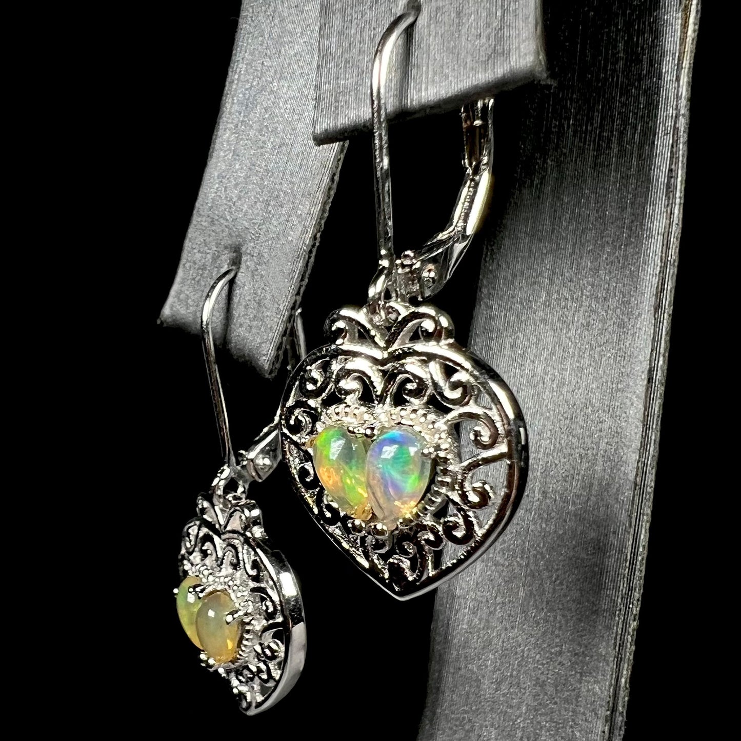 A pair of dangling sterling silver filigree heart earrings, each set with two Ethiopian opals.