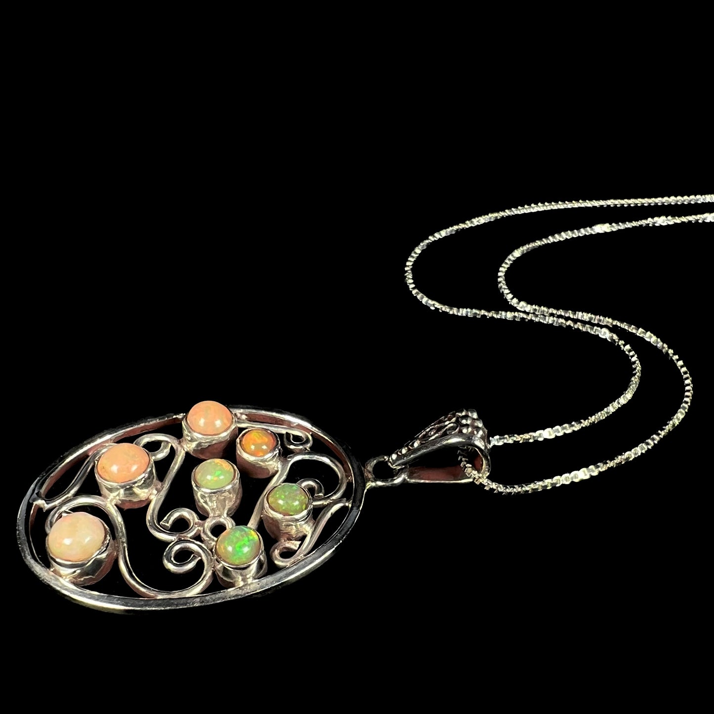 An Ethiopian opal filigree necklace shown at an angled view, laying on a black background.