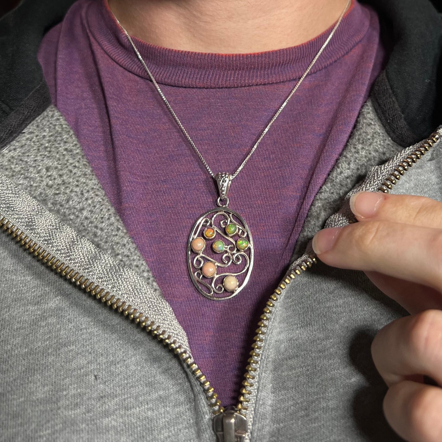 A sterling silver Ethiopian opal filigree necklace worn around a neck and shown against a purple shirt.