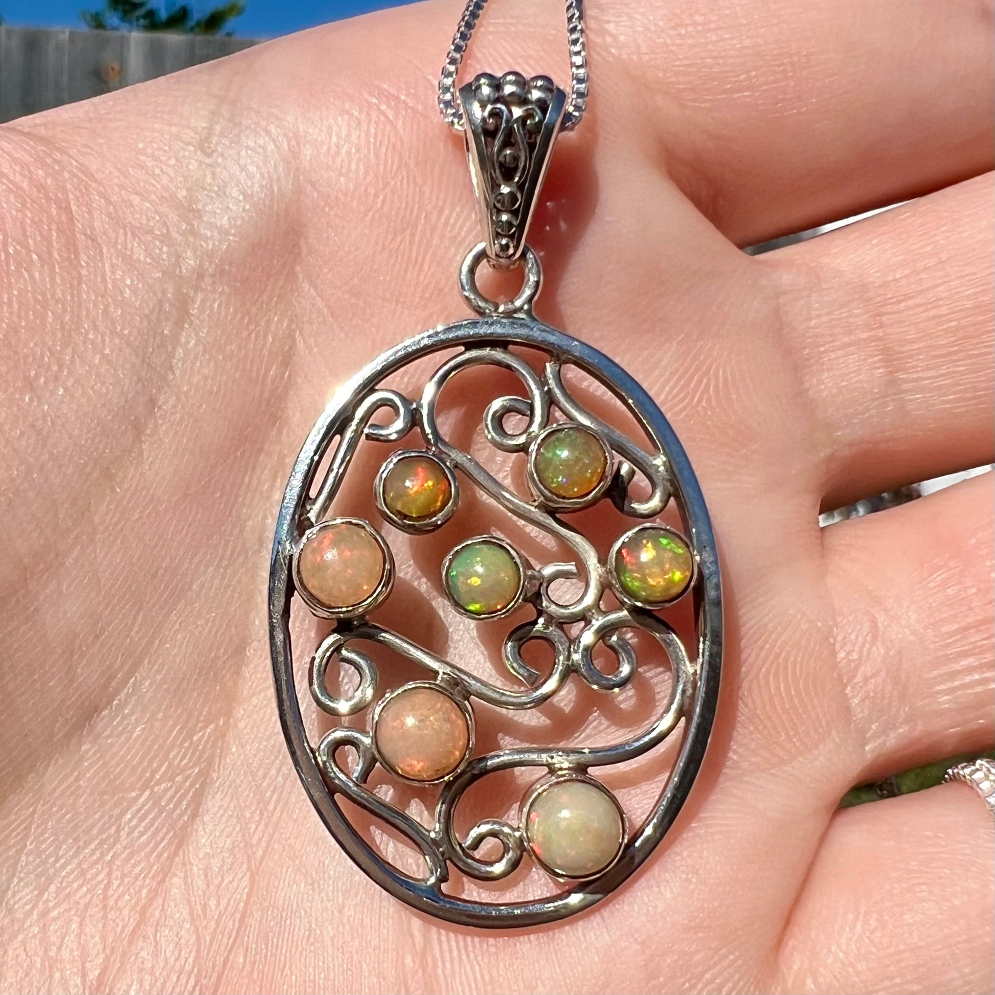 A sterling silver Ethiopian opal filigree necklace shown close-up in a hand in sunlight.