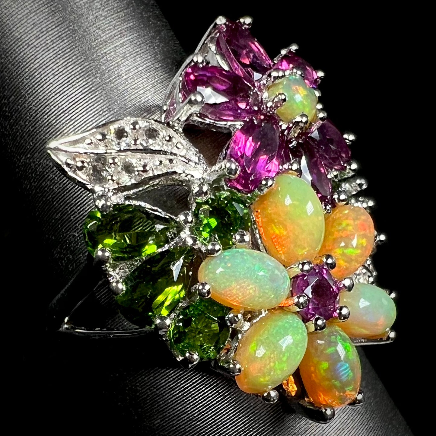 An Ethiopian opal flower ring set with garnets, chrome diopside, and white topaz, shown at an angle.
