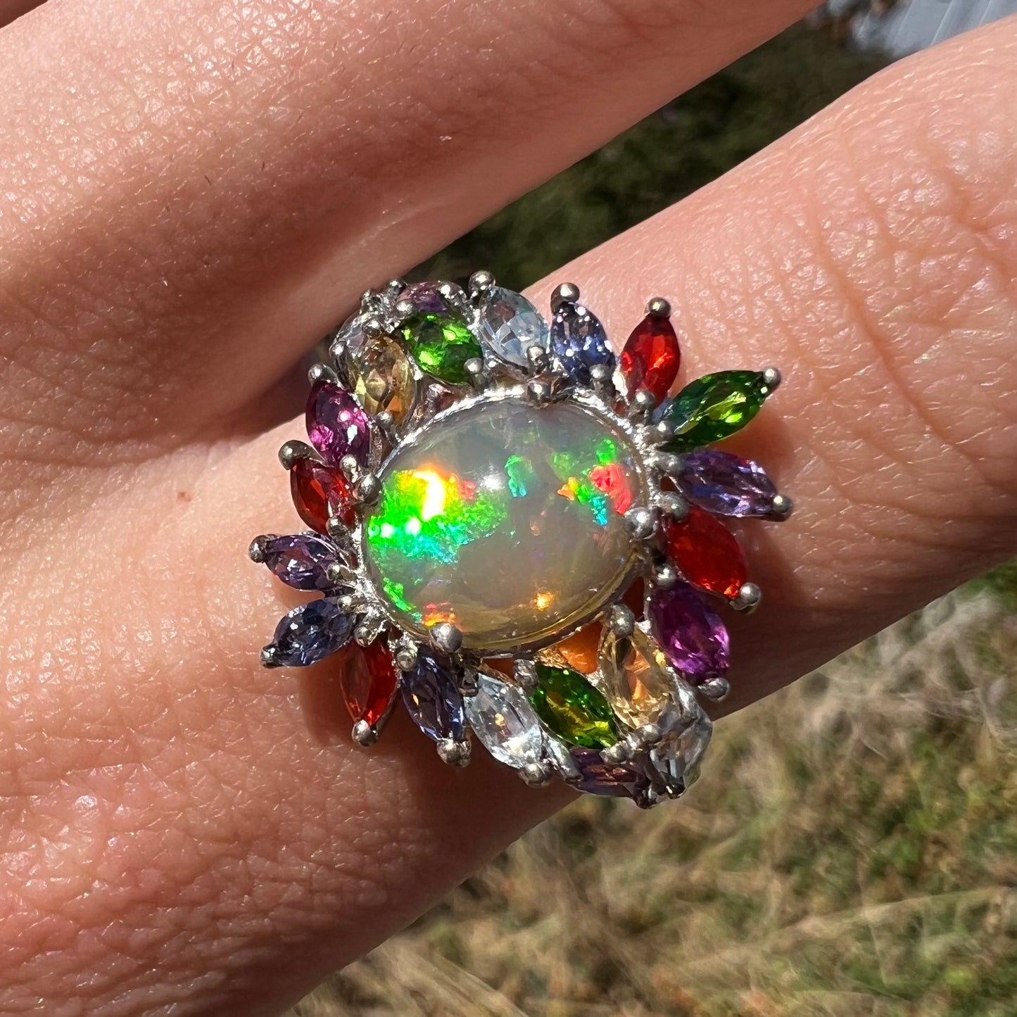 Front close-up of an Ethiopian opal fruit salad ring, worn on a finger and shown in natural sunlight.
