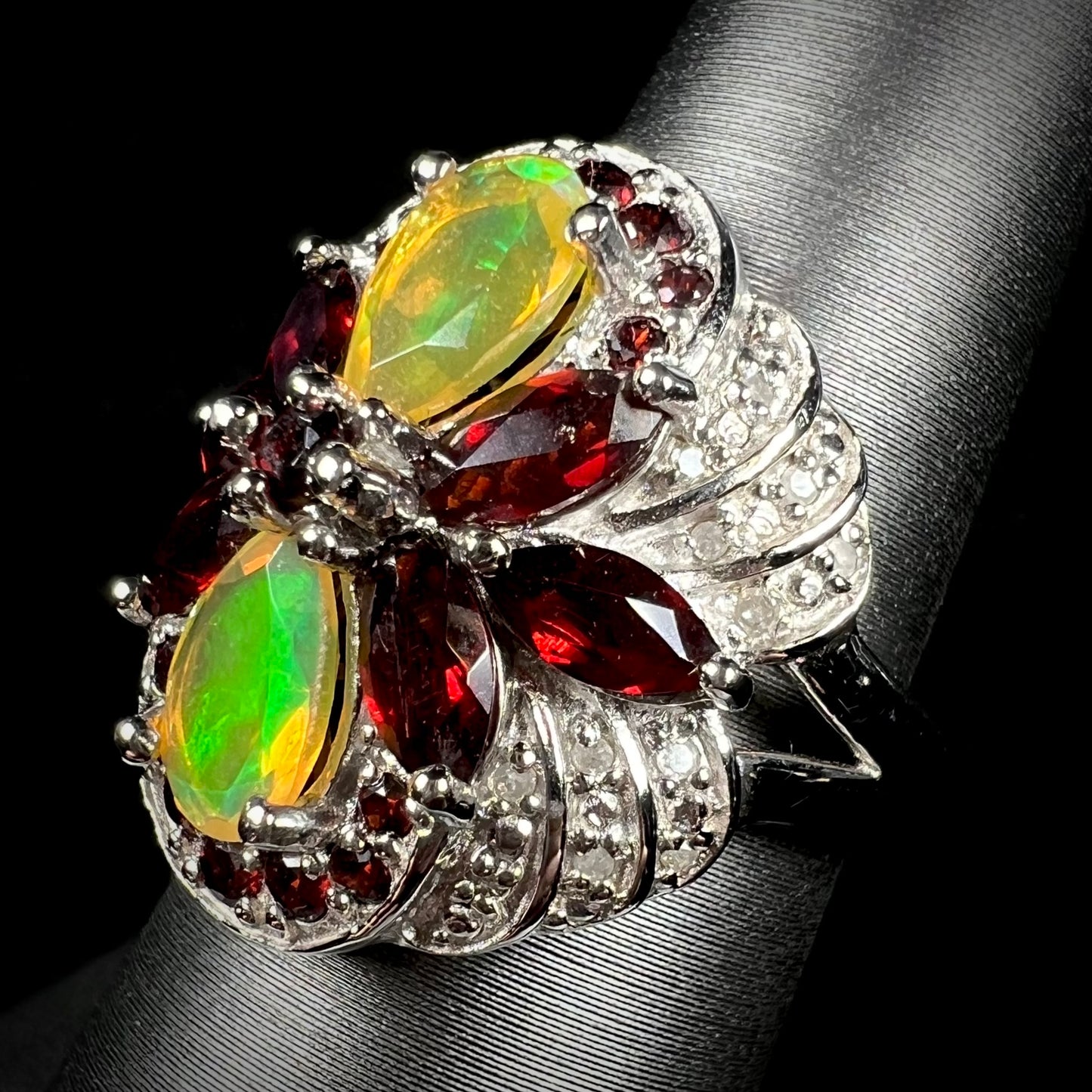 An Ethiopian opal, garnet, and diamond ring in silver, shown from an angle.