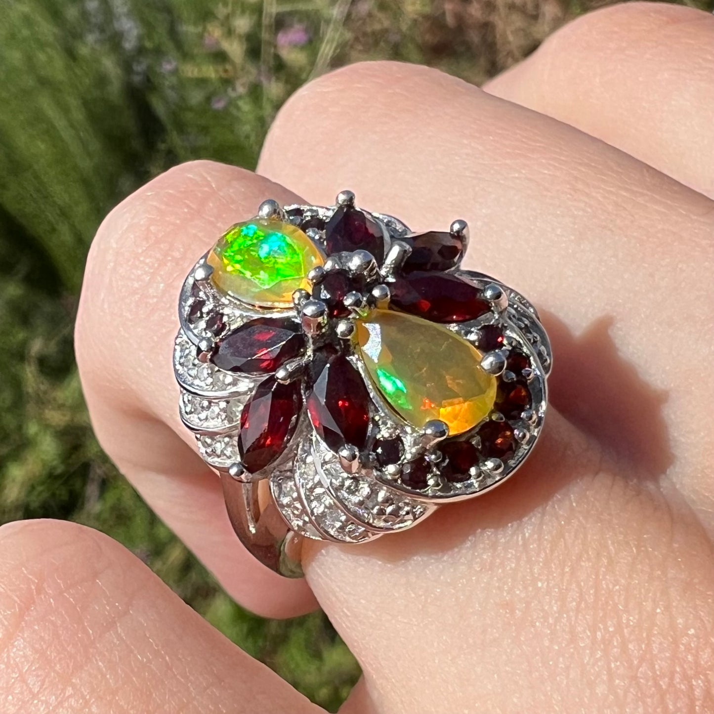 Angled sunlit view of a sterling silver Ethiopian opal and garnet infinity-design ring with diamond accents.
